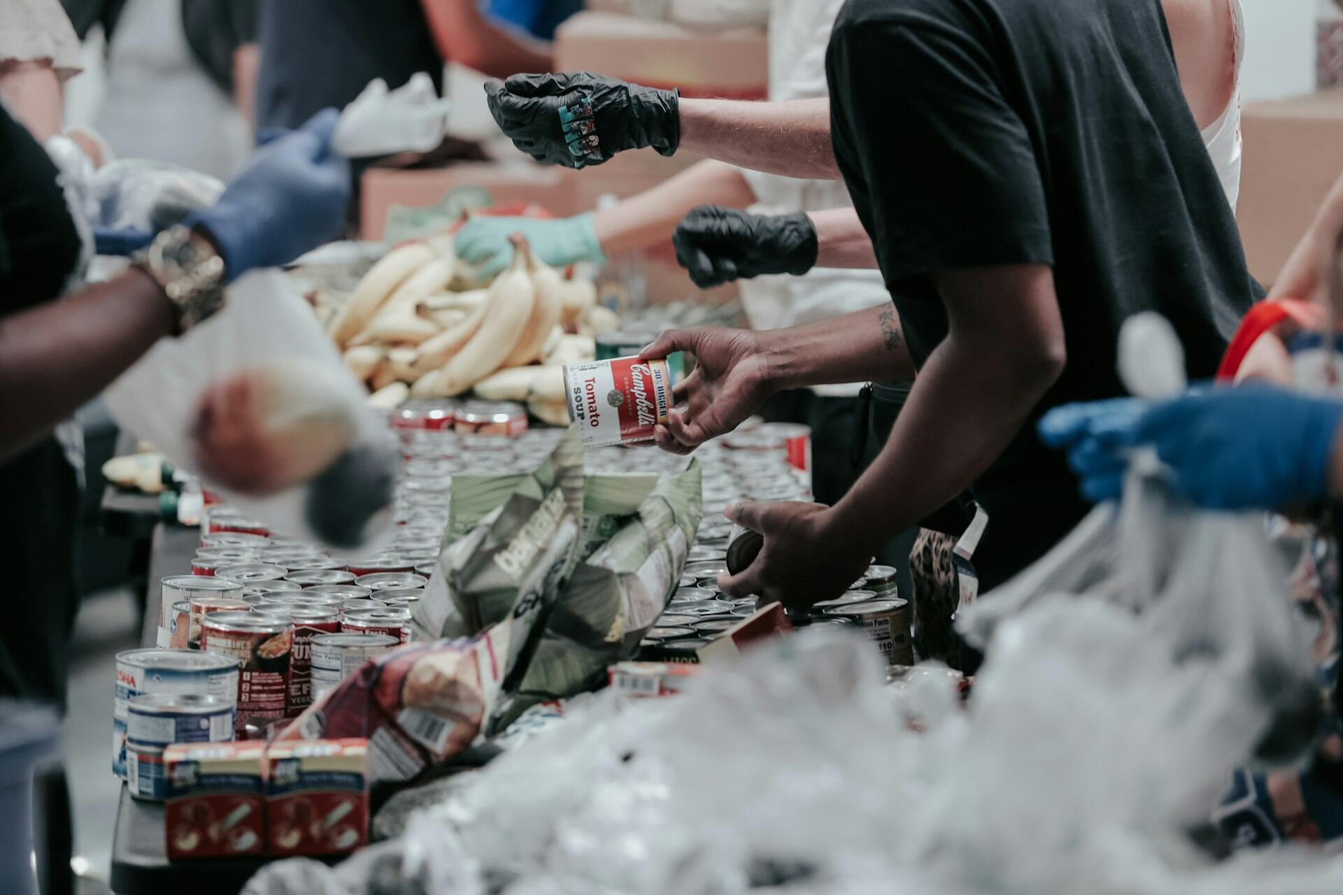 People wearing gloves sort and distribute food items, including canned goods and bananas, at a community food pantry.