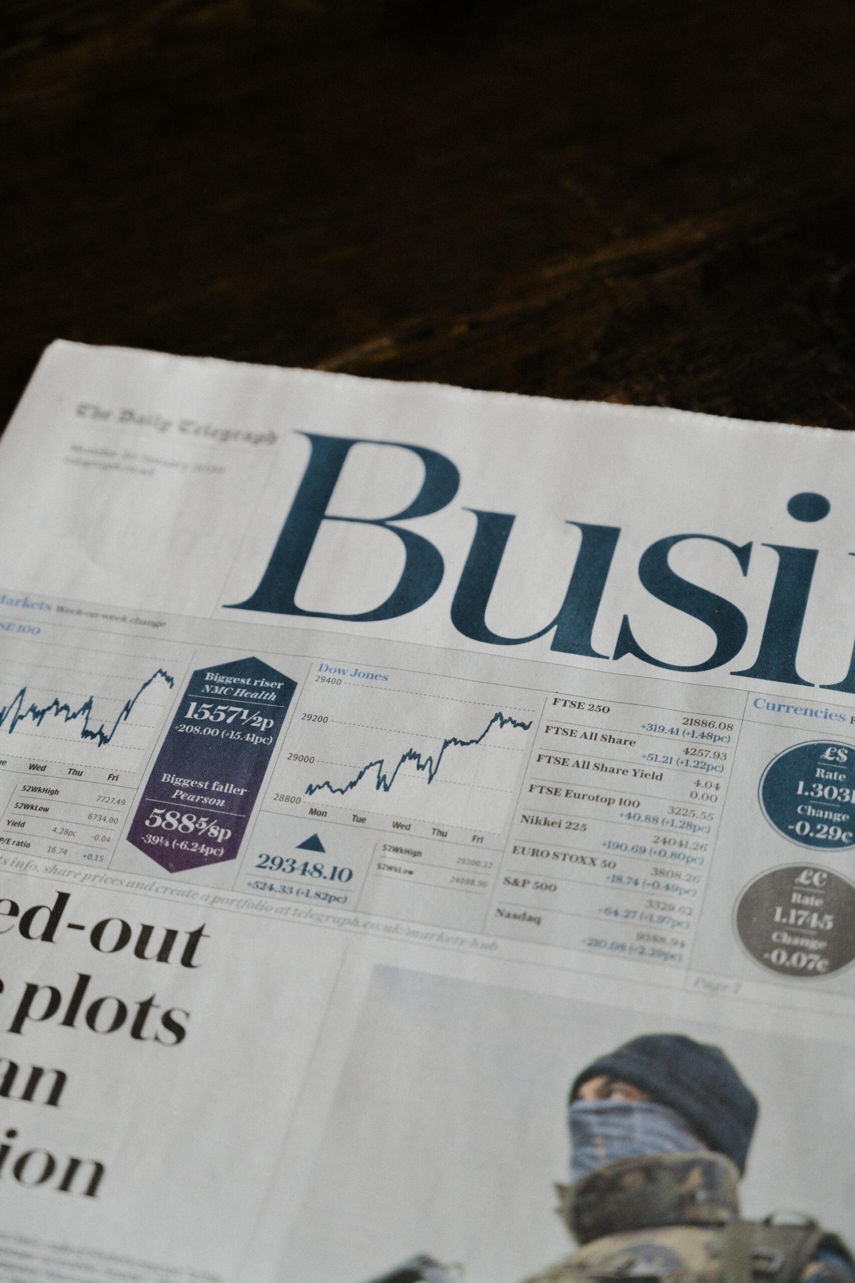A close-up of a business newspaper featuring stock market charts, headlines, and economic data, resting on a wooden surface.