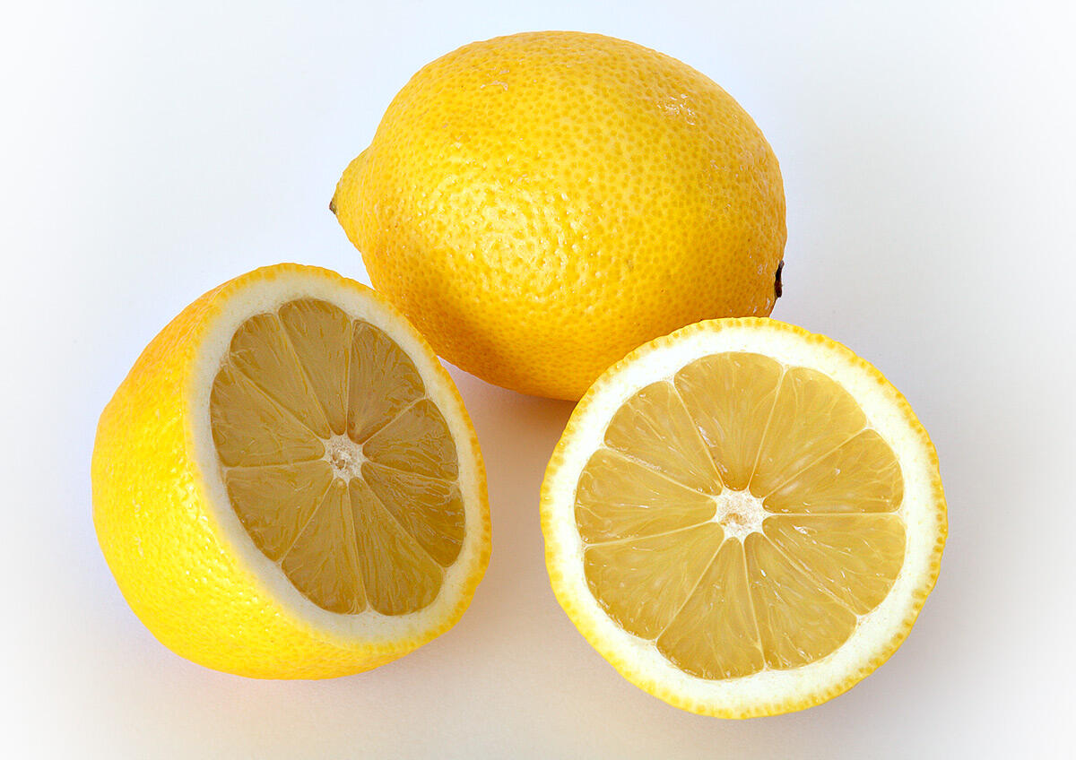 Whole and halved yellow lemons on a white surface, showing juicy interior and textured skin.