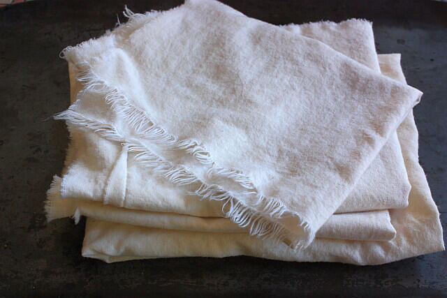 Stack of soft, white muslin fabric with frayed edges on a dark surface.