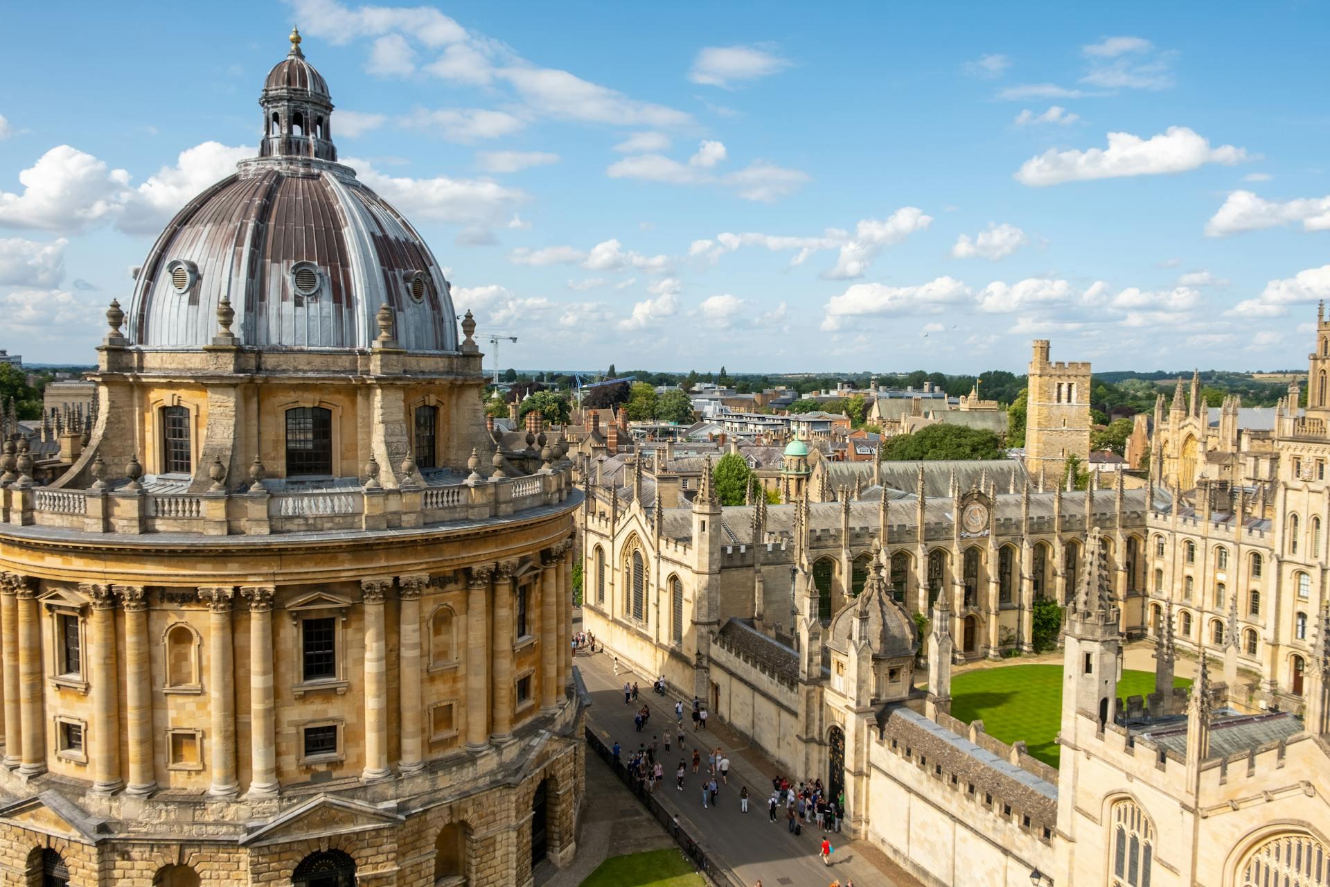 Aerial view of Oxford University, showcasing historic buildings and a prominent dome under a blue sky with scattered clouds.