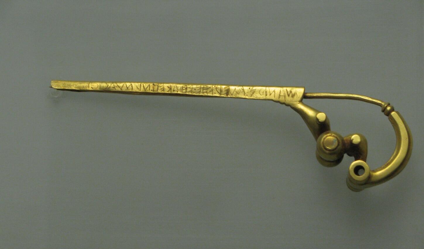 Golden hairpin with an ornate design and inscriptions along the length, showcasing intricate craftsmanship from a historical period.