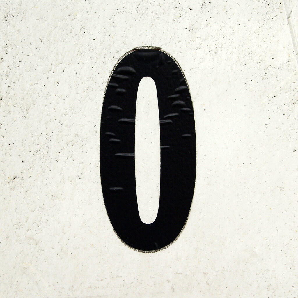 Black number zero on a textured white wall.