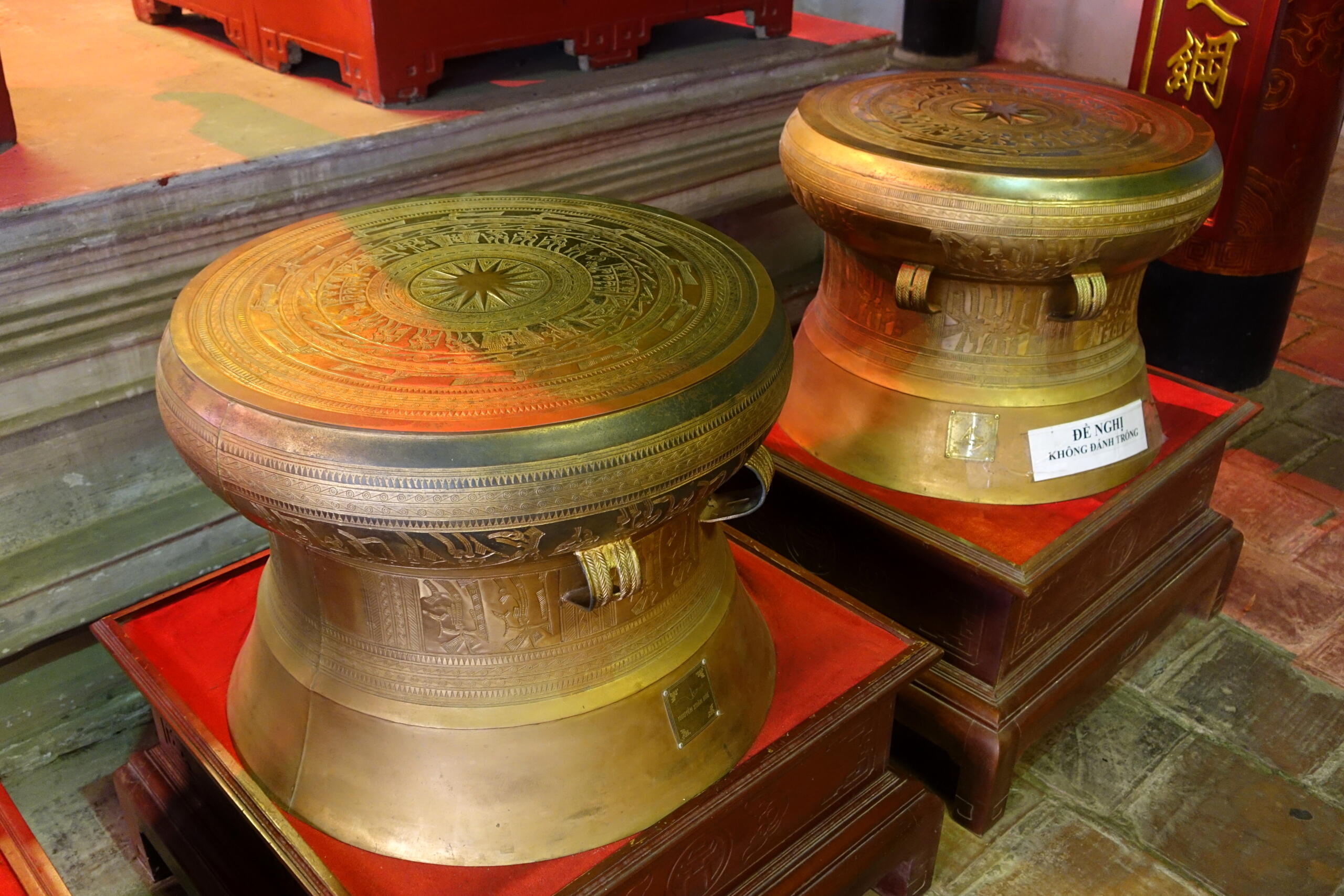 Ancient bronze Dong Son drums from Vietnam displayed in a museum with intricate carvings.