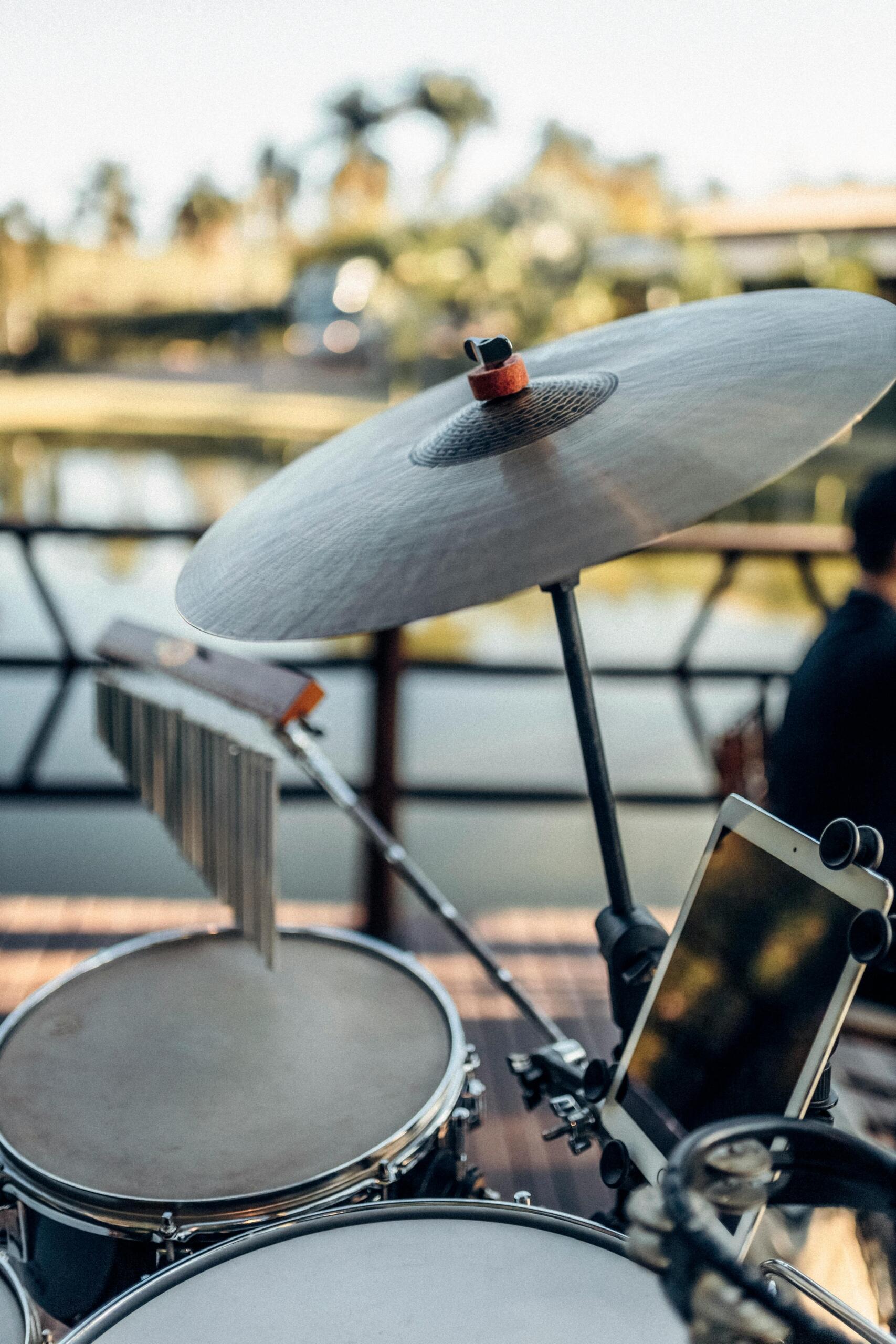 crash cymbals positioned on a rod above a drumset in an outdoor setting.