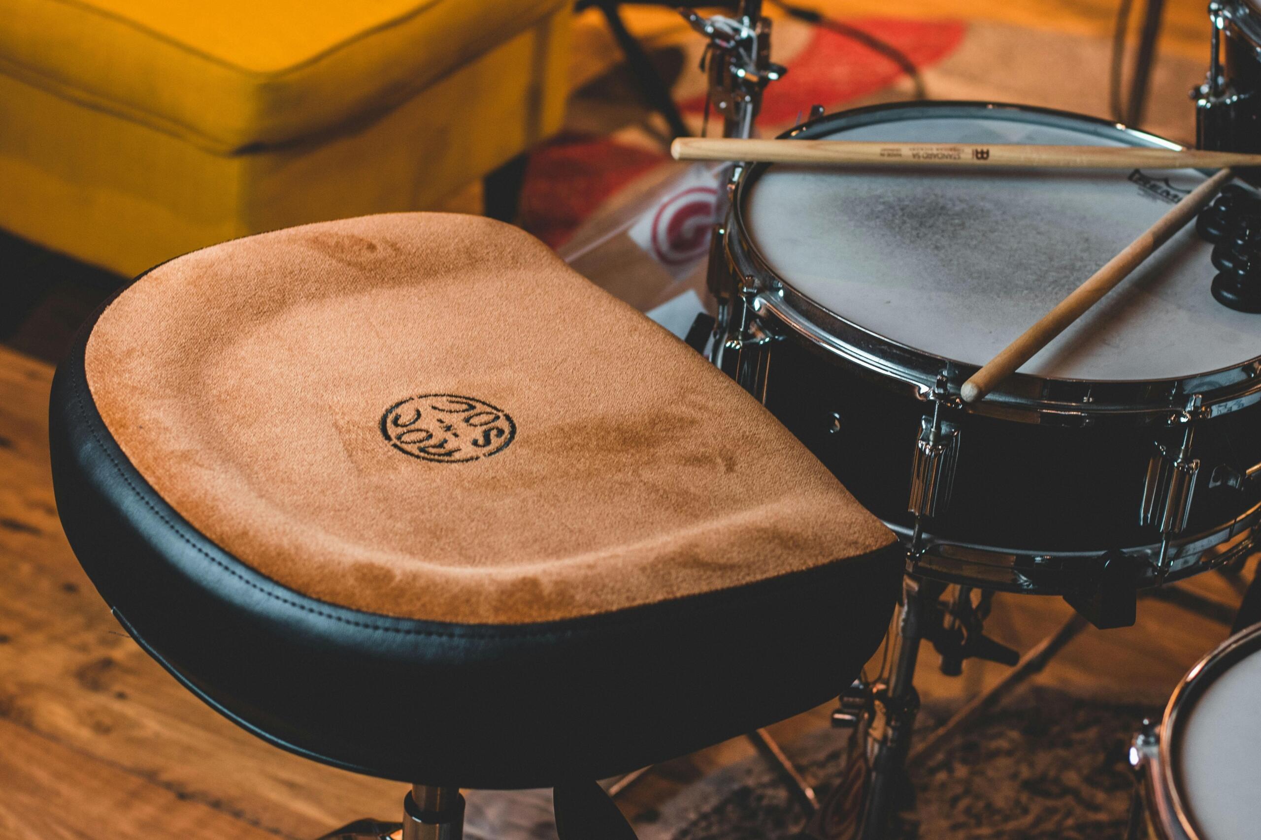 Adjustable drum throne with padded seat and sturdy metal base, designed for drummers’ comfort and posture during long sessions.