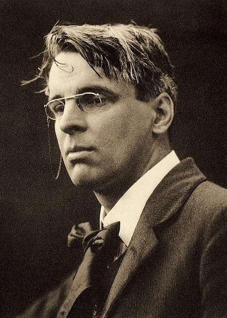 A sepia-toned portrait of William Butler Yeats, the Irish poet, wearing round glasses and a suit, with slightly tousled hair.