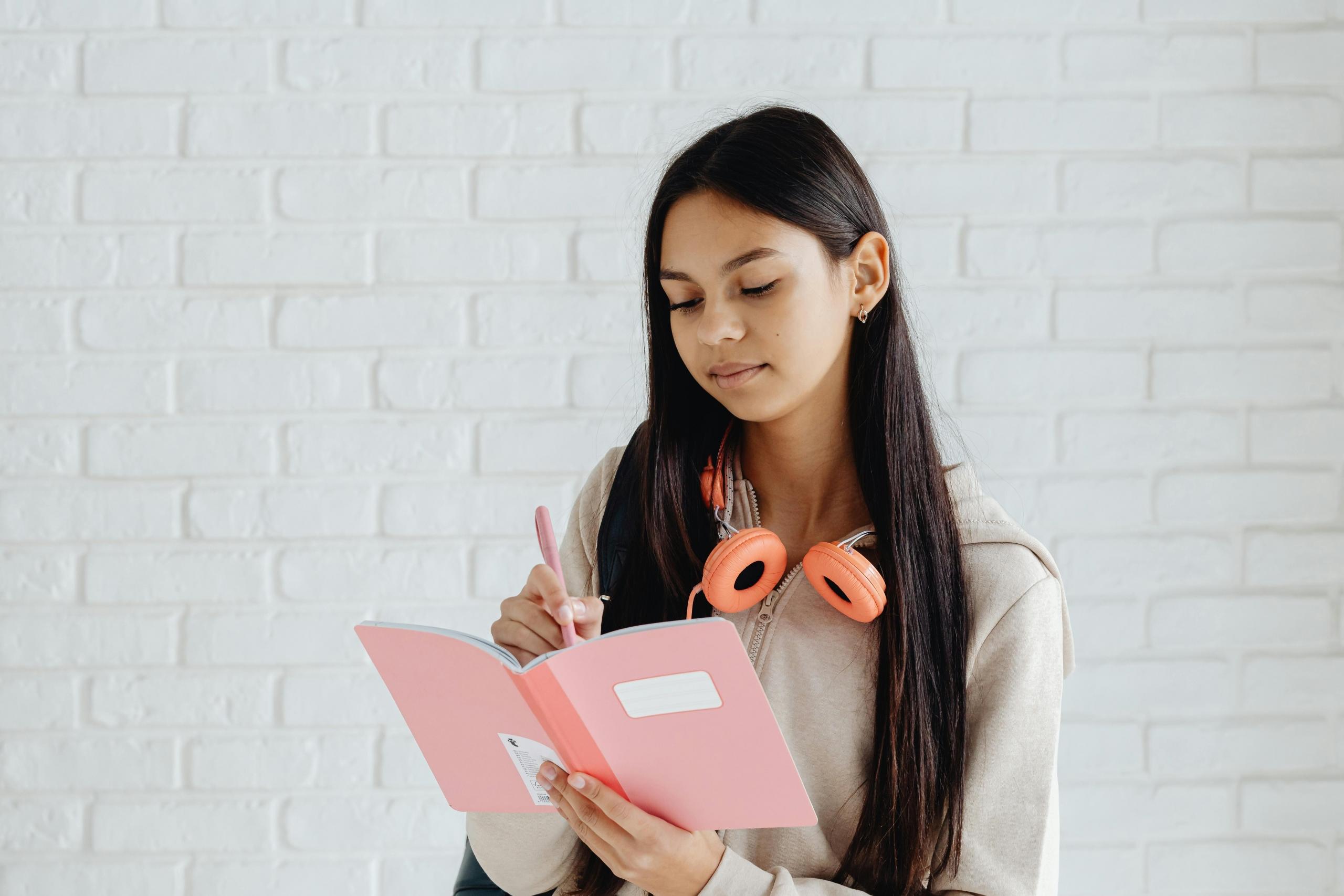 A girl going over her notes with a pink notebook and headphones.