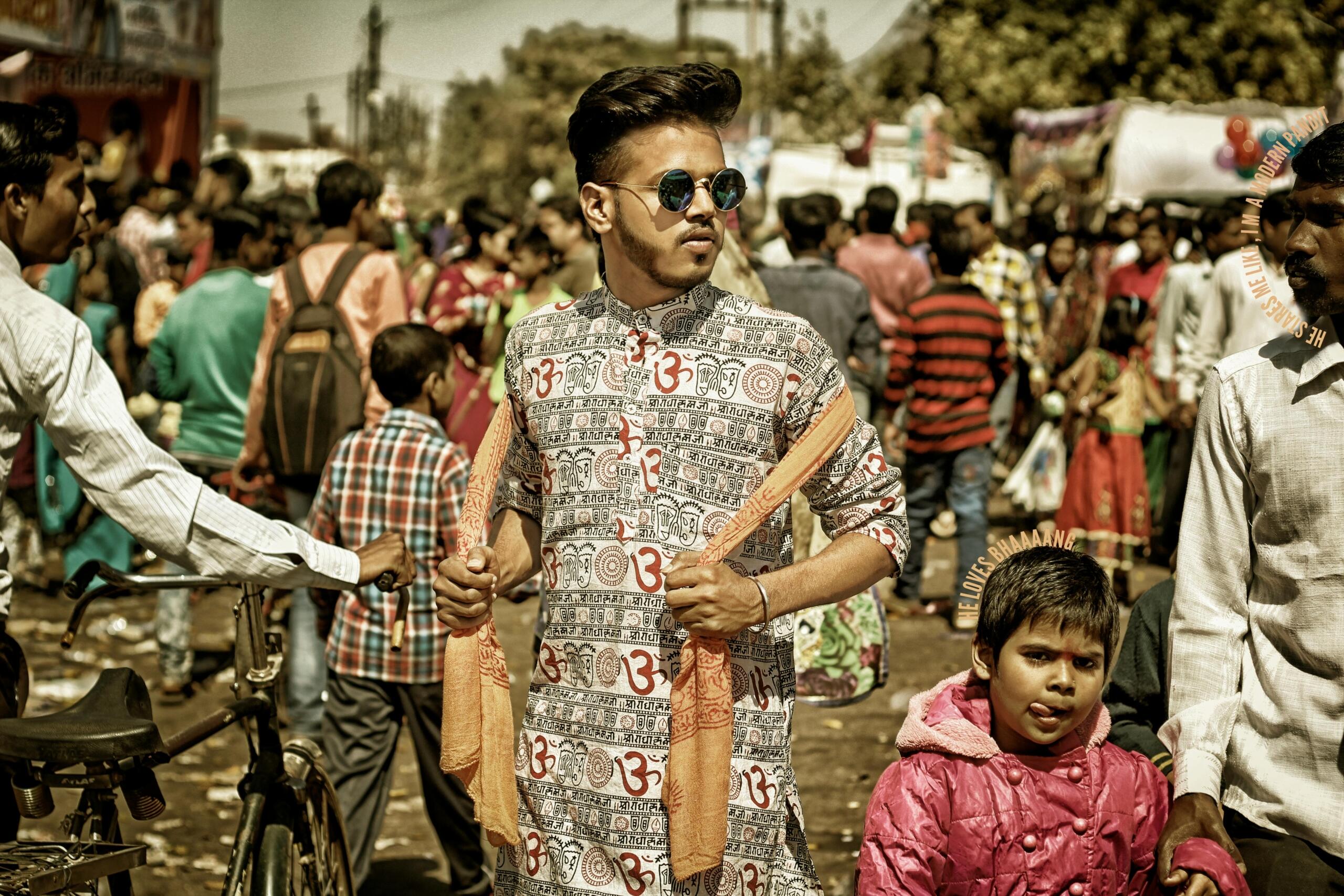 Indian man standing in the middle of a busy crowd in India, surrounded by people and colorful street activity.