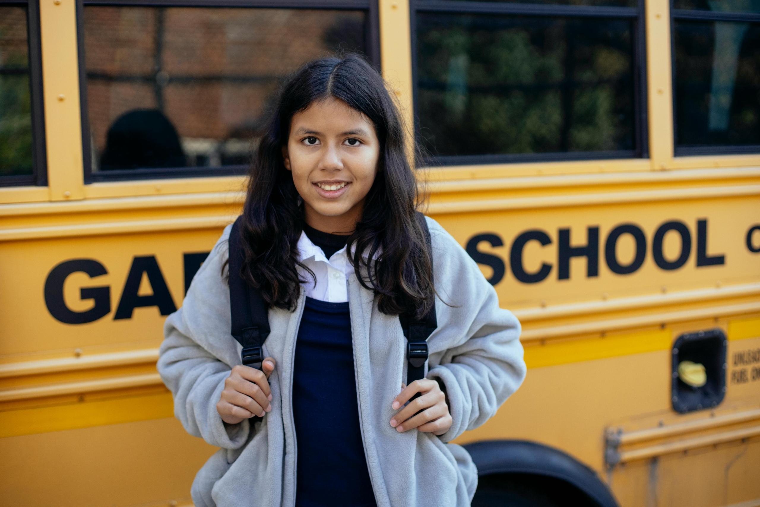 A Latin American girl standing infront a school bus.