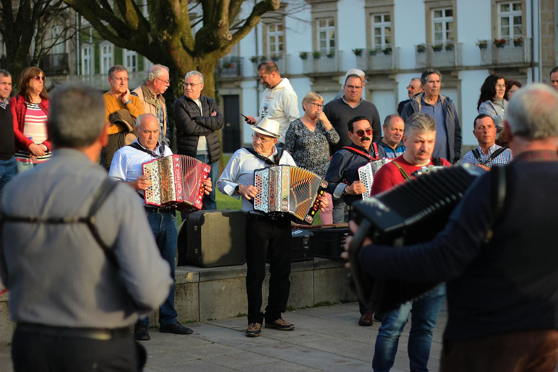 A group of musicians plays accordions in a vibrant outdoor setting, surrounded by an engaged audience of onlookers.