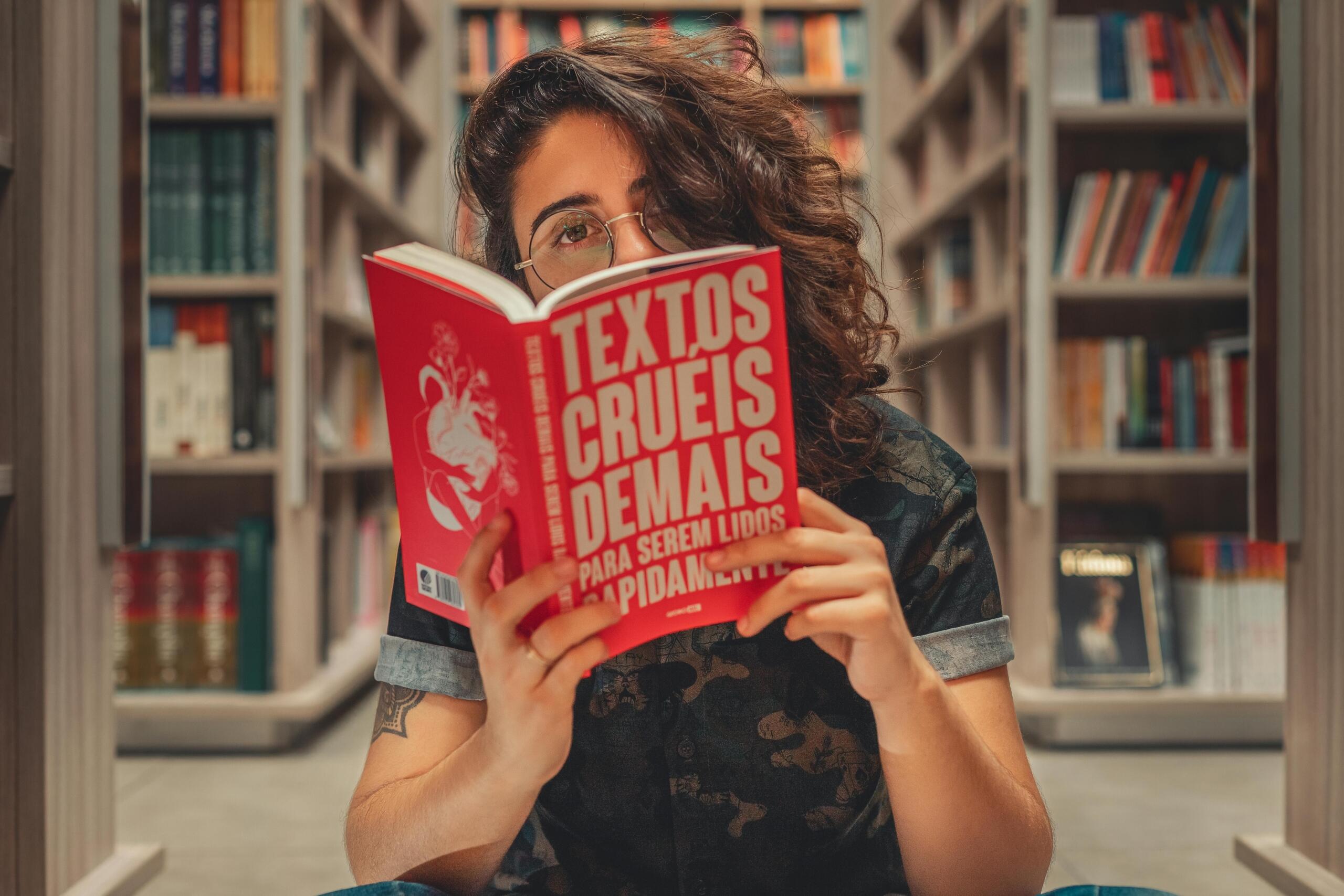 A woman is in a bookstore. She holds a red book with Portuguese writing on it.