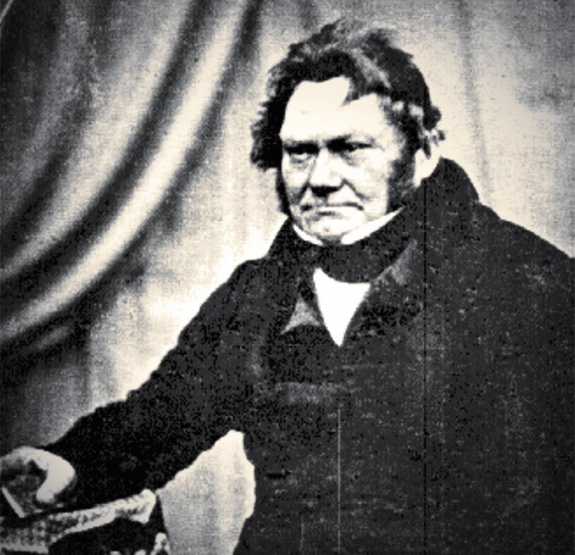 a black and white photo of a man in a suit. The man has a stern expression.