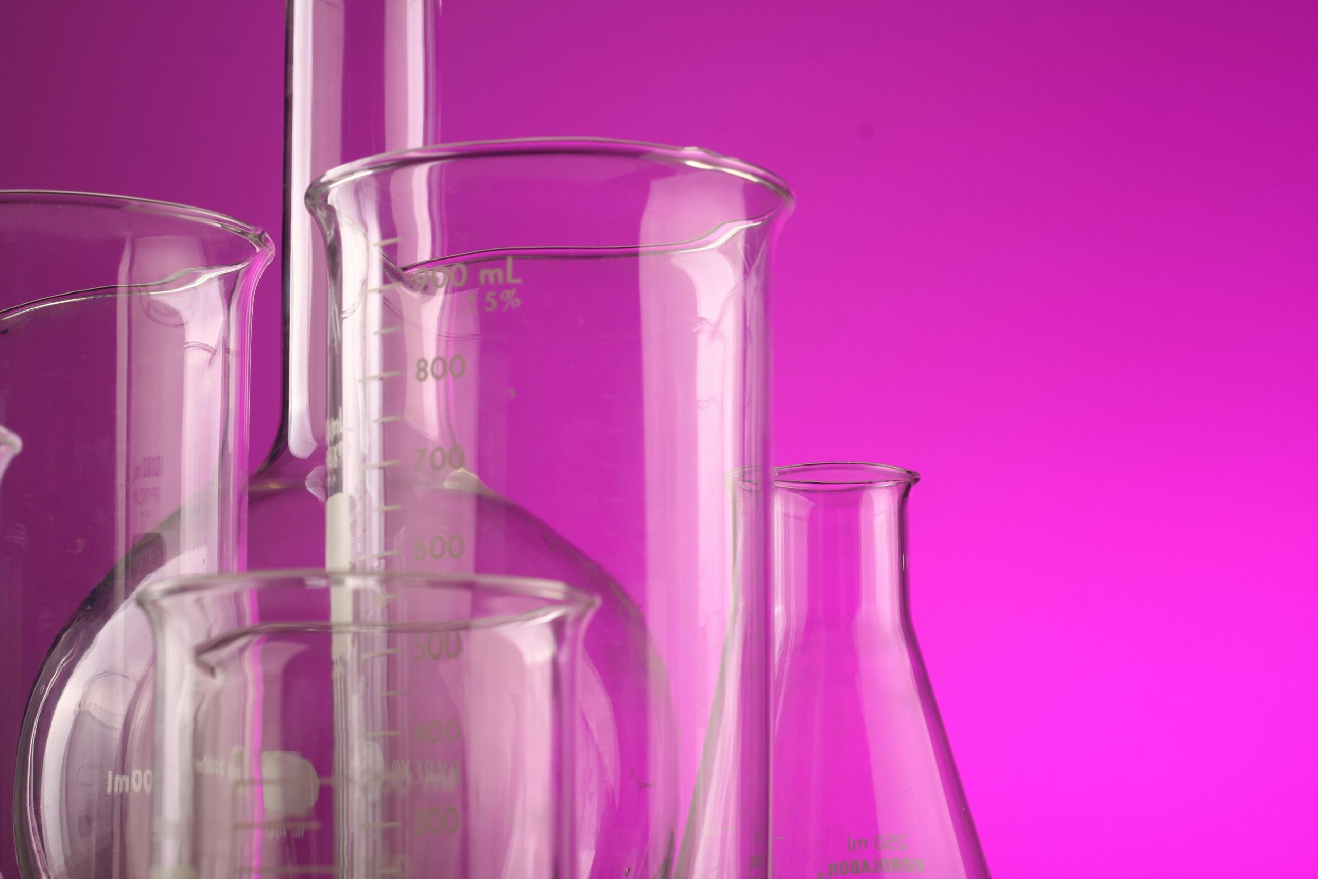 a set of glass scientific beakers and containers in front of a bright purple background.