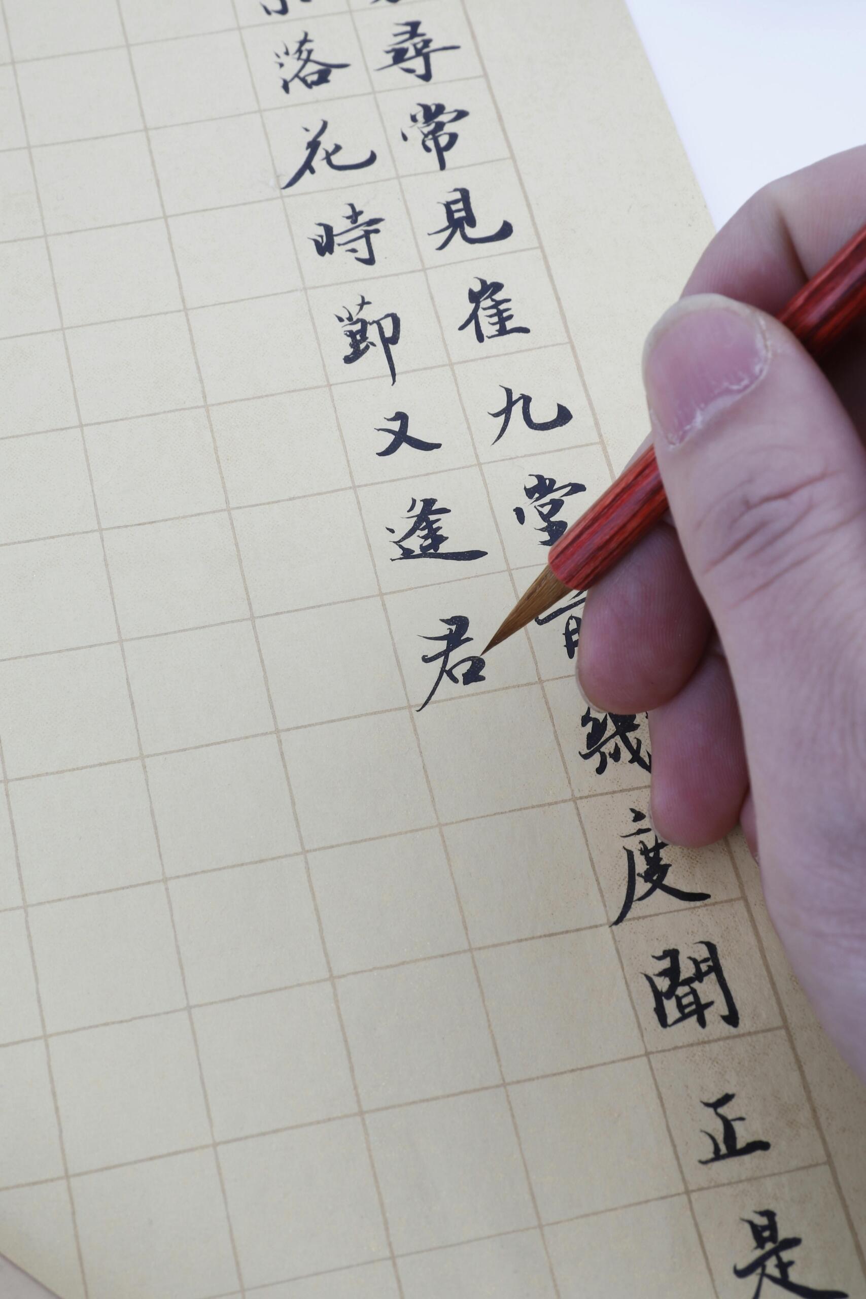 A close-up of a hand holding a pen, writing Chinese characters on lined paper with neat, flowing strokes.
