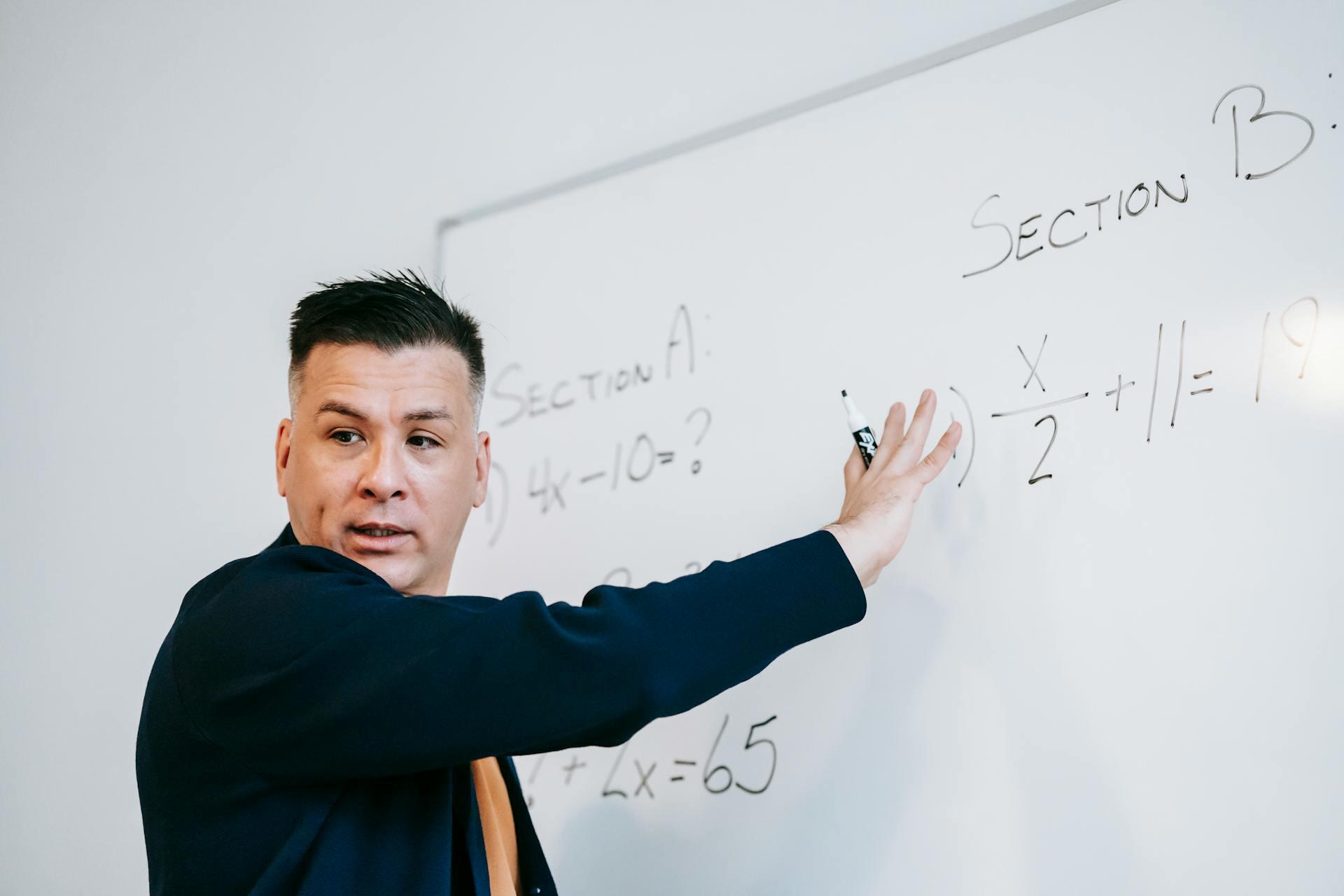 Teacher solving algebra problems on a whiteboard, writing equations labeled Section A and Section B.