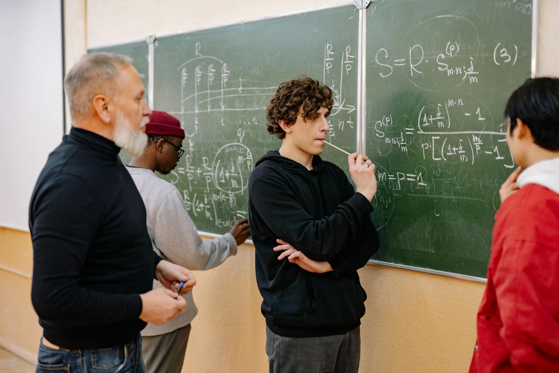 Group of people solving complex mathematical equations on a chalkboard in a classroom setting.