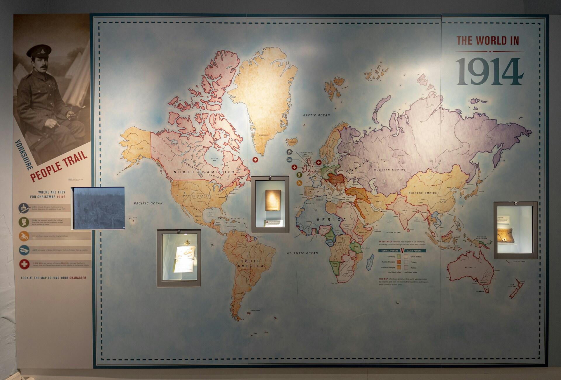 World map from 1914 showing empires and alliances with display cases and a soldier's photo on the left.