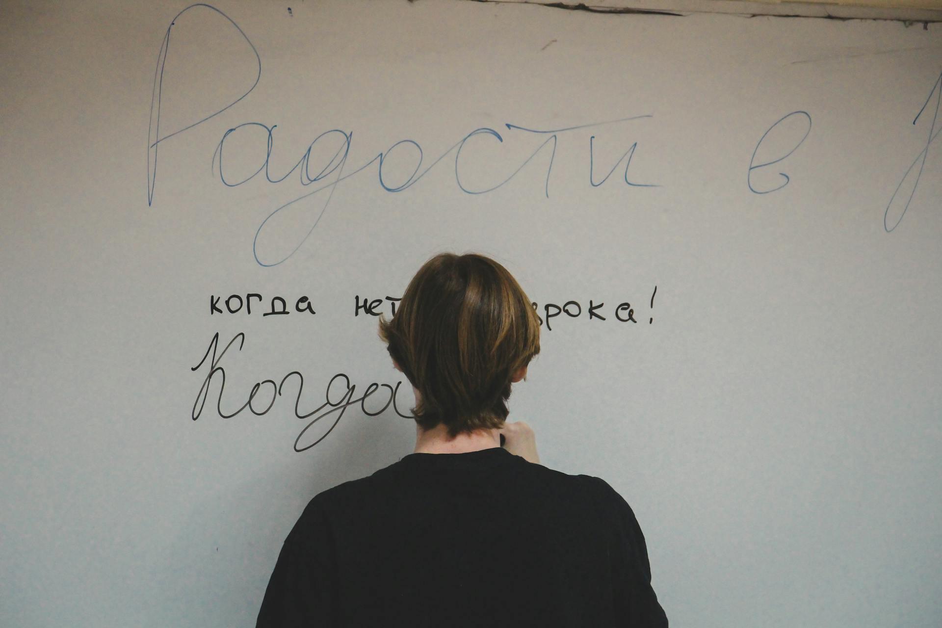 A person with shoulder-length hair writes on a wall, including phrases in Russian about joy and freedom from lessons.