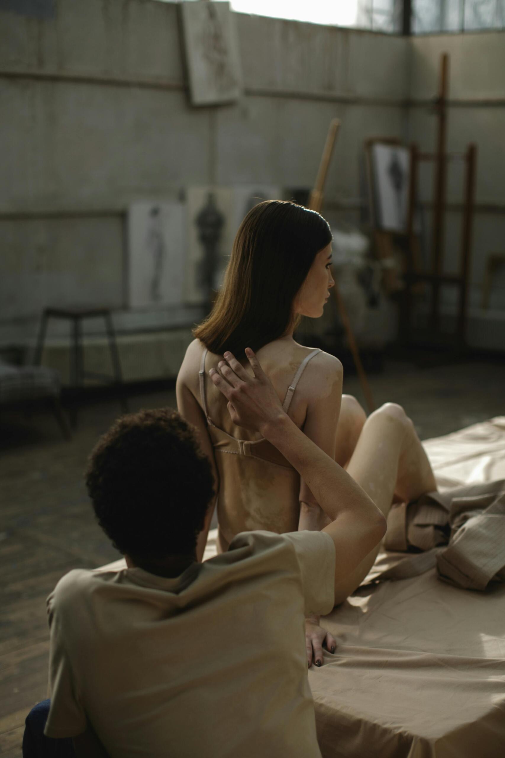 A life drawing model posing in the foreground while an artist behind her raises his hand to visually measure proportions for his sketch. Source: Cottonbro Studio.