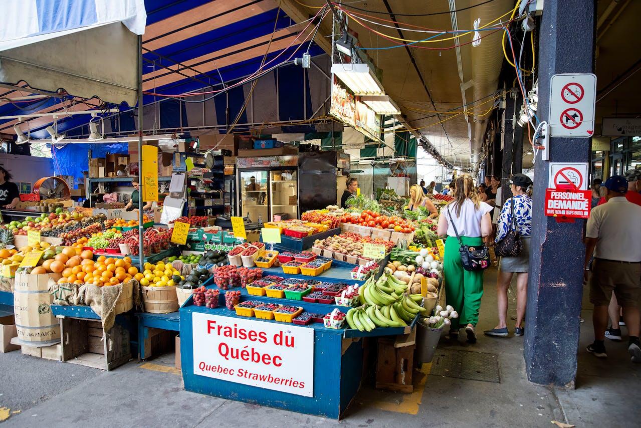 A vibrant market scene filled with colorful fruits and vegetables, shoppers browsing, and stalls adorned with signs in French.