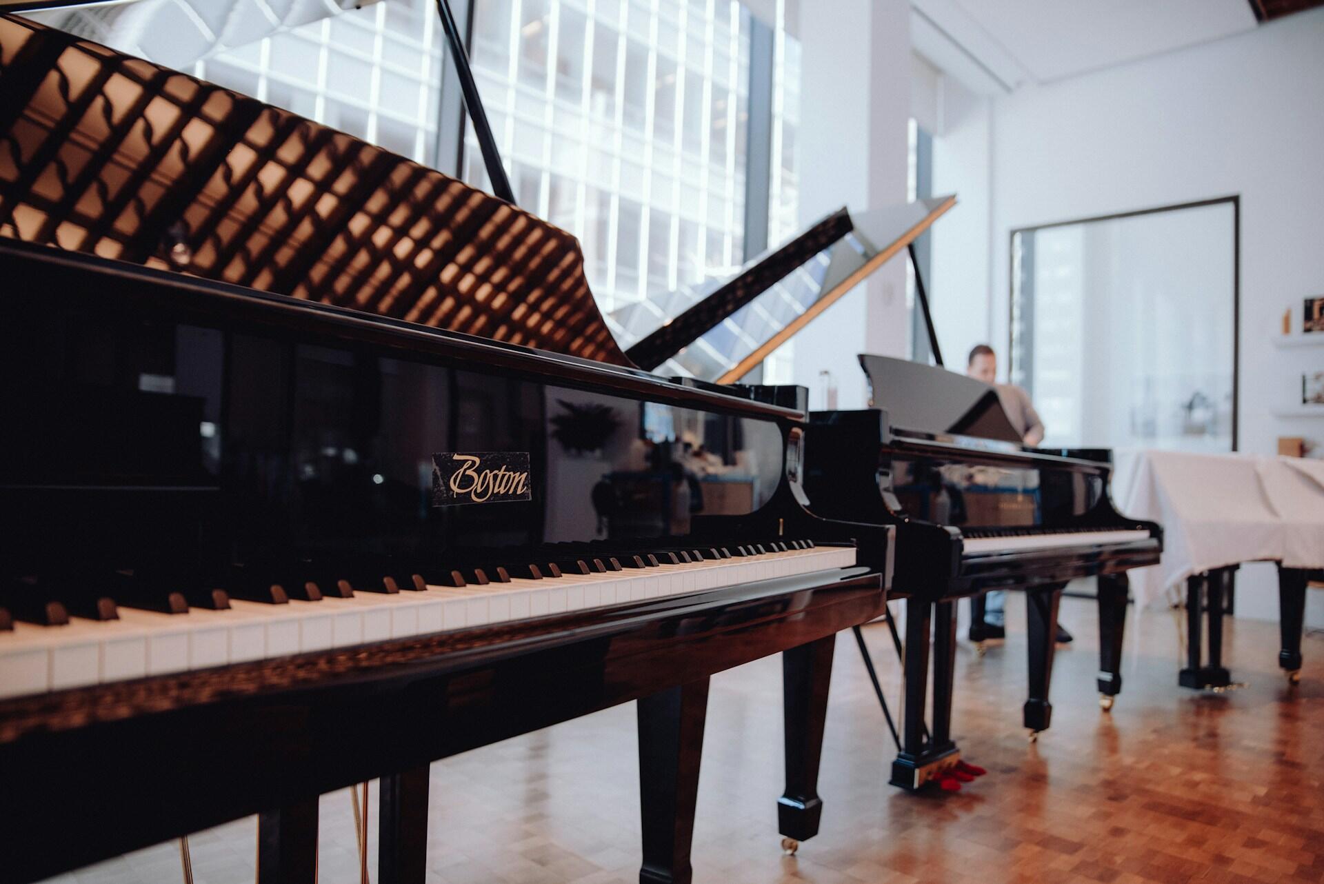 Two elegant grand pianos are displayed in a bright, modern music studio with large windows, showcasing a lively urban view.