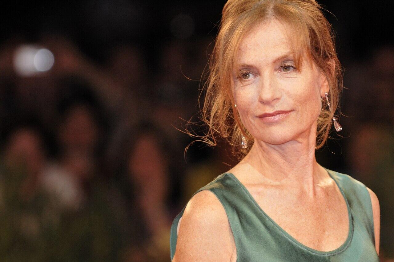 Woman in a green sleeveless dress at an event, with blurred crowd and dim lighting in the background.