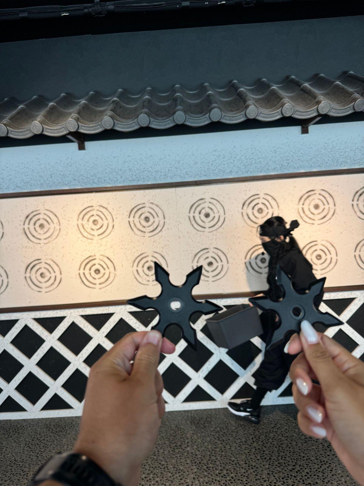Two people holding ninja stars at a target wall inside the Ninja and Samurai Museum in Japan.
