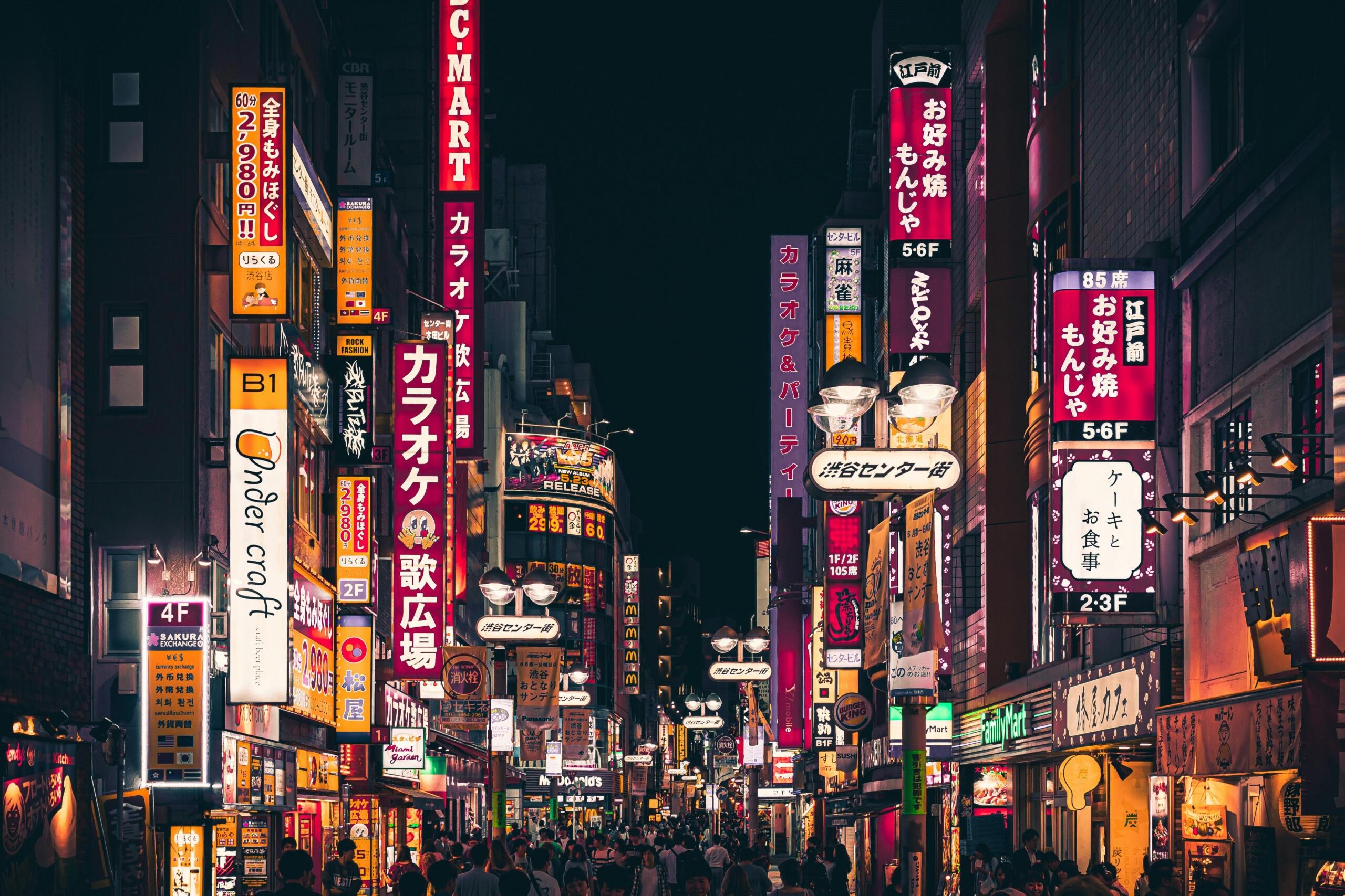 Bustling street in Shinjuku, Tokyo at night with colorful neon signs and crowds of people.