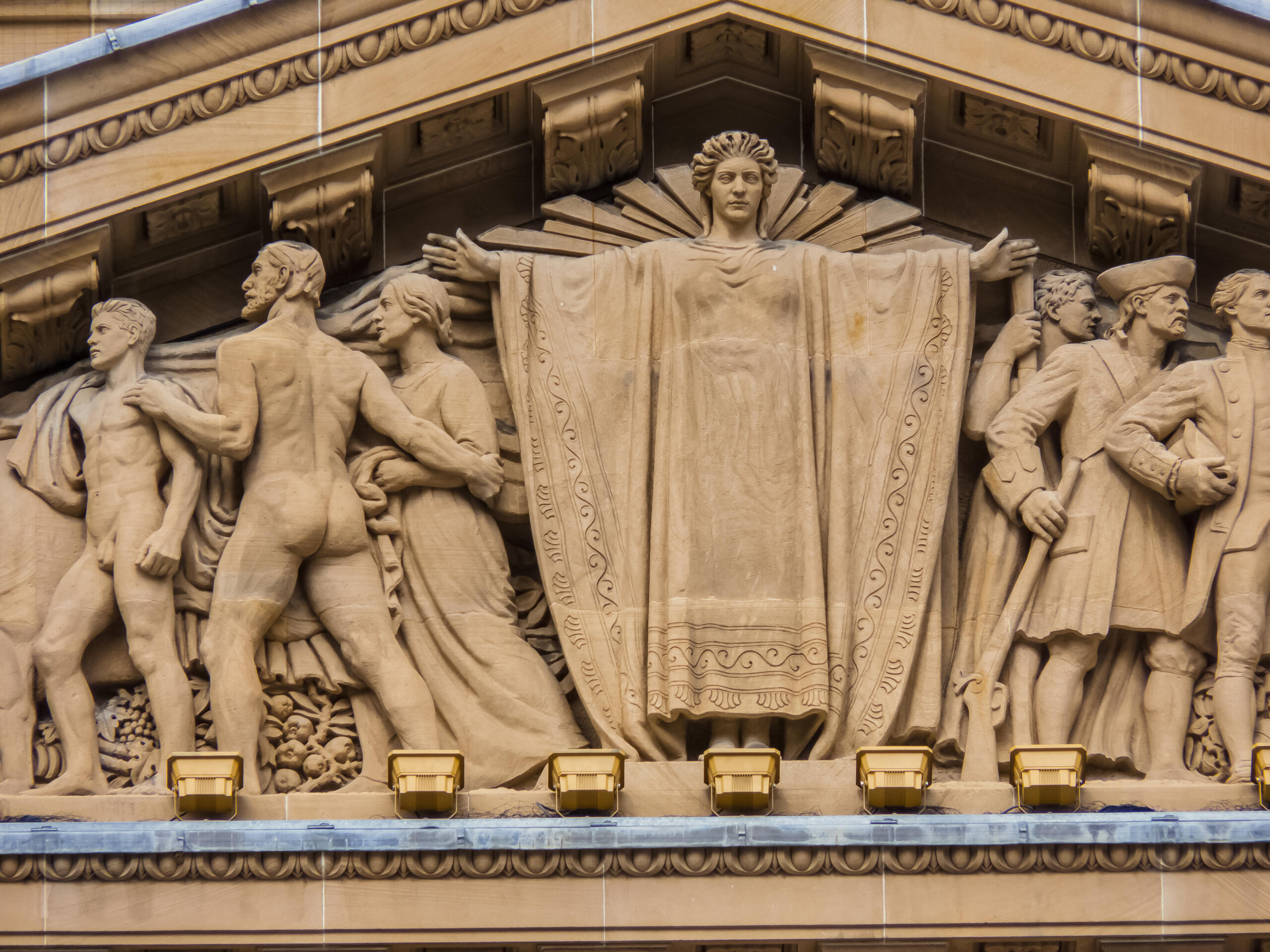 Stone relief sculpture depicting historical and allegorical figures on a classical building façade.