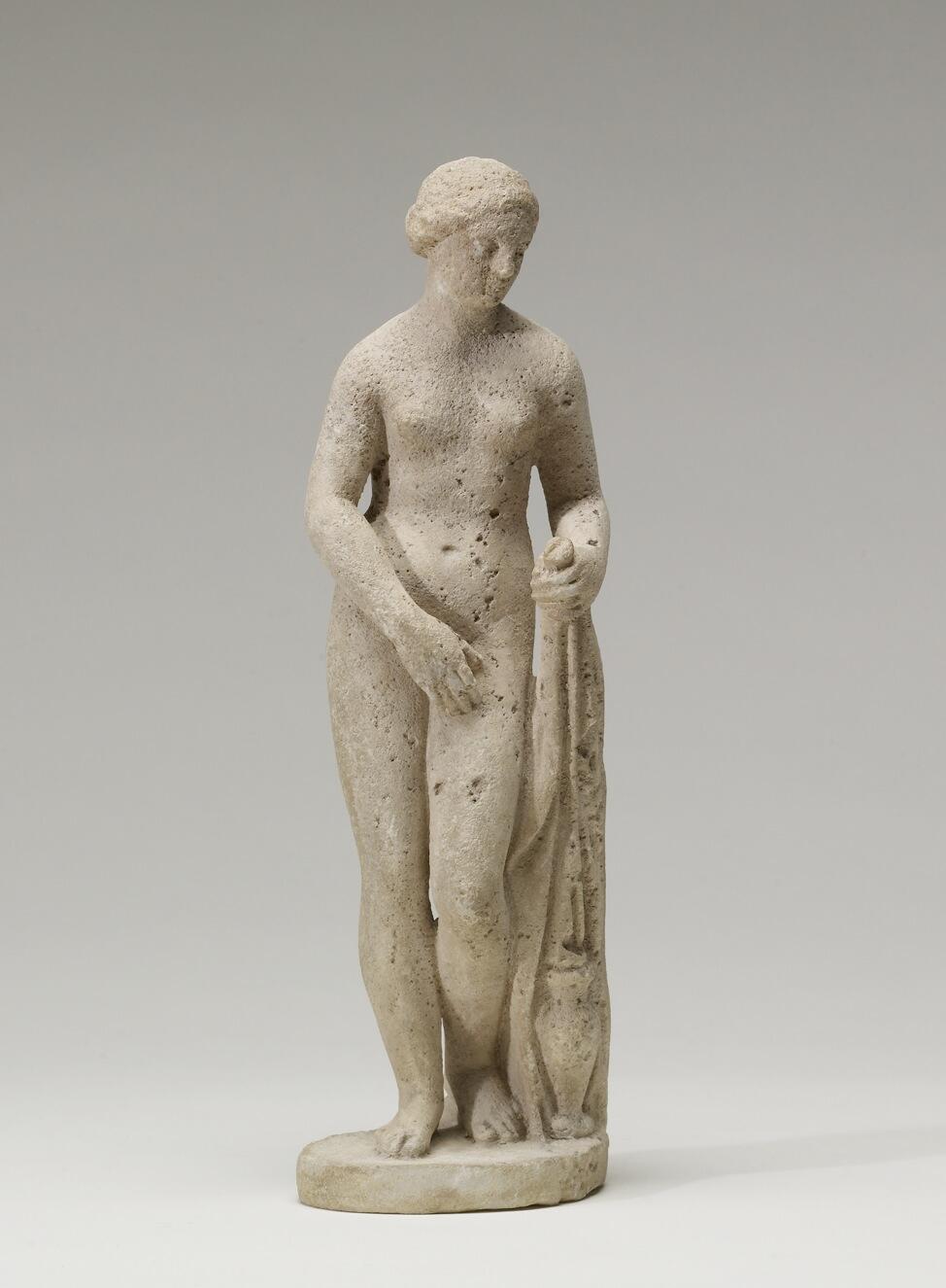 Marble statue of Aphrodite of Cnidus in a graceful contrapposto pose beside a draped garment.