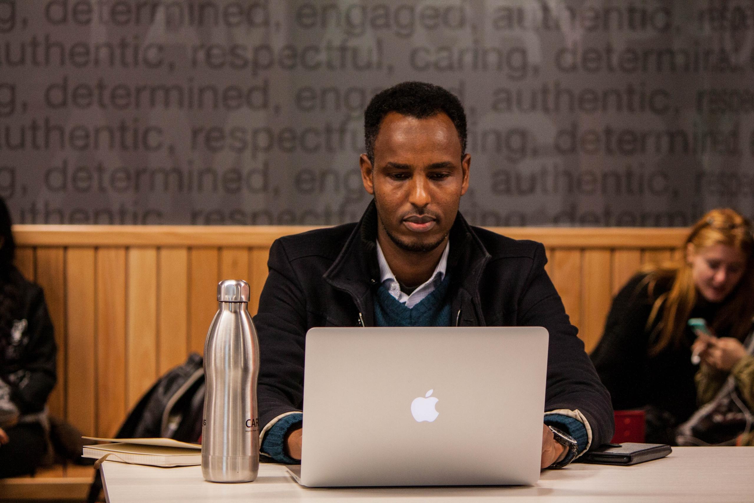 A man works at a computer in a classroom.