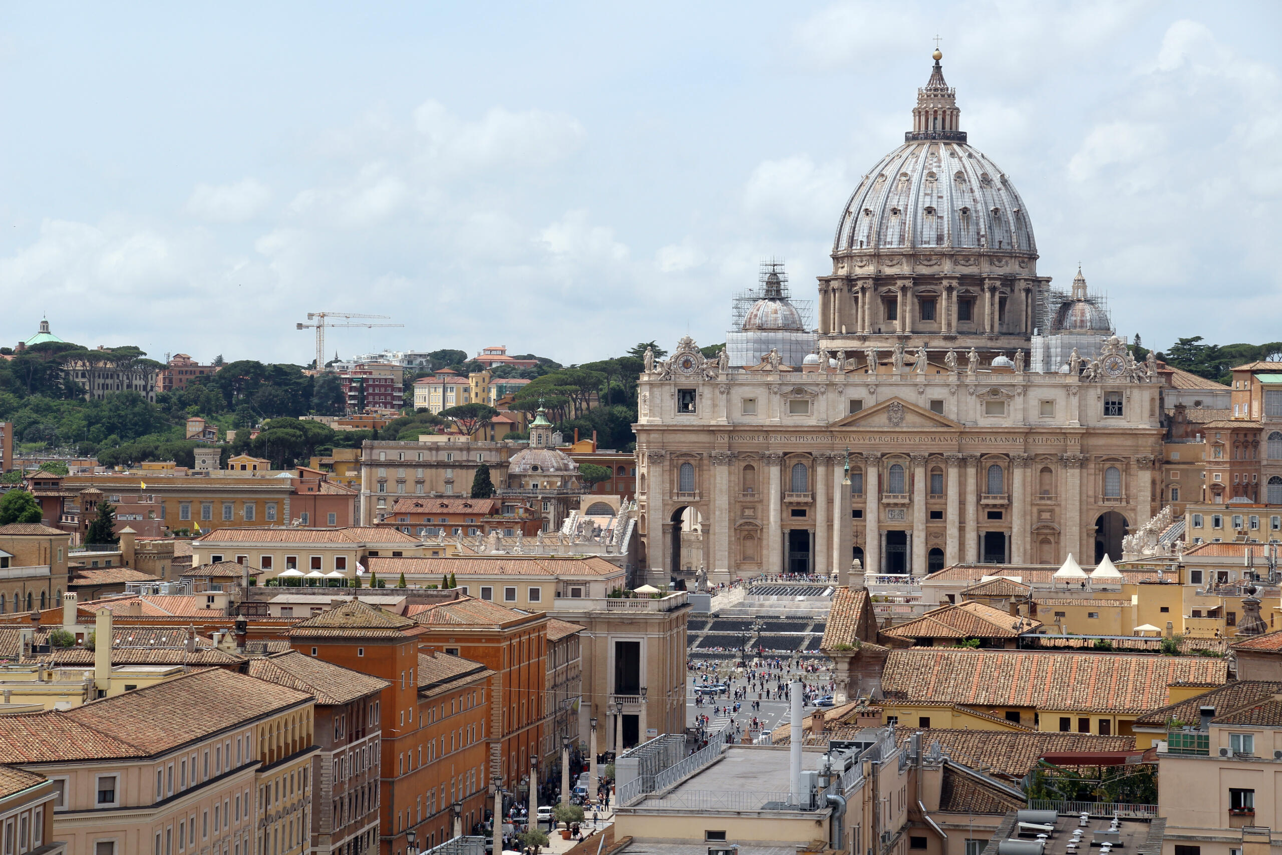 During the day, St. Peter's Basilica stands imposingly over Rome's urban landscape, standing out for its monumental dome and white travertine facade that reflects the sunlight. From a distance, its silhouette dominates the city's architecture, surrounded by historic buildings, ochre rooftops, and streets that preserve the ancient layout of the Italian capital.