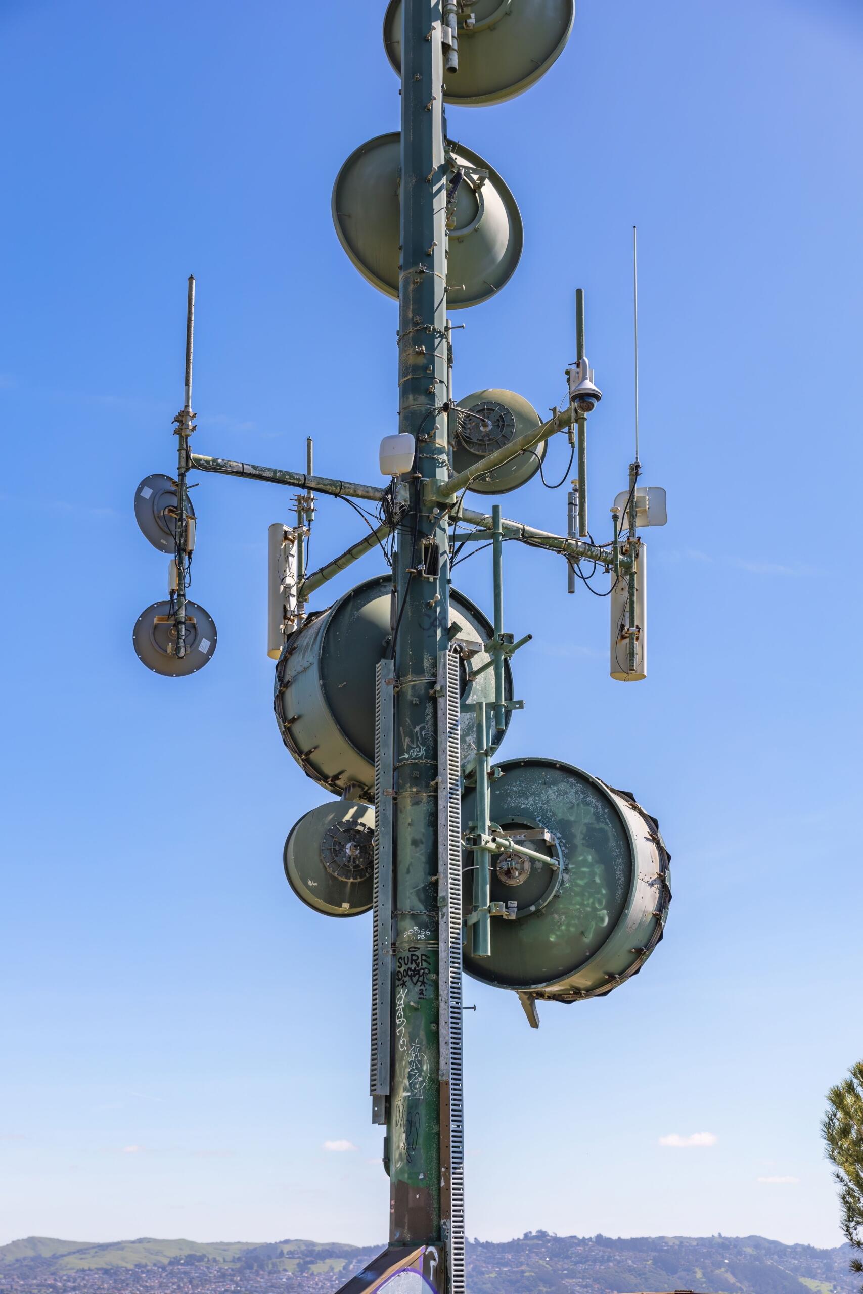 Tall cell phone tower fitted with multiple antennas and communication equipment against the sky.