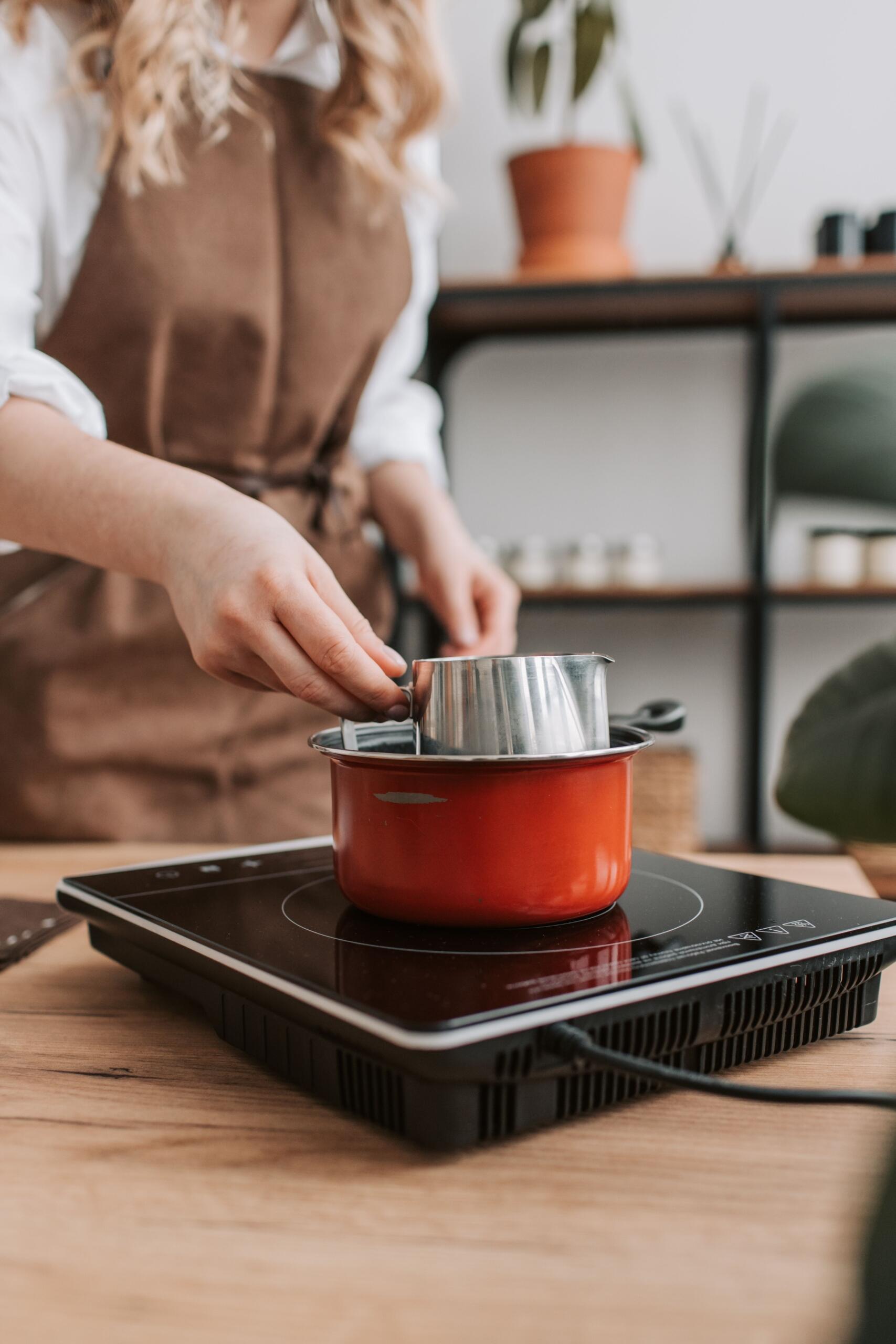 A woman prepares a meal on an induction cooktop in a modern kitchen, stirring food in a pot on the smooth cooking surface.