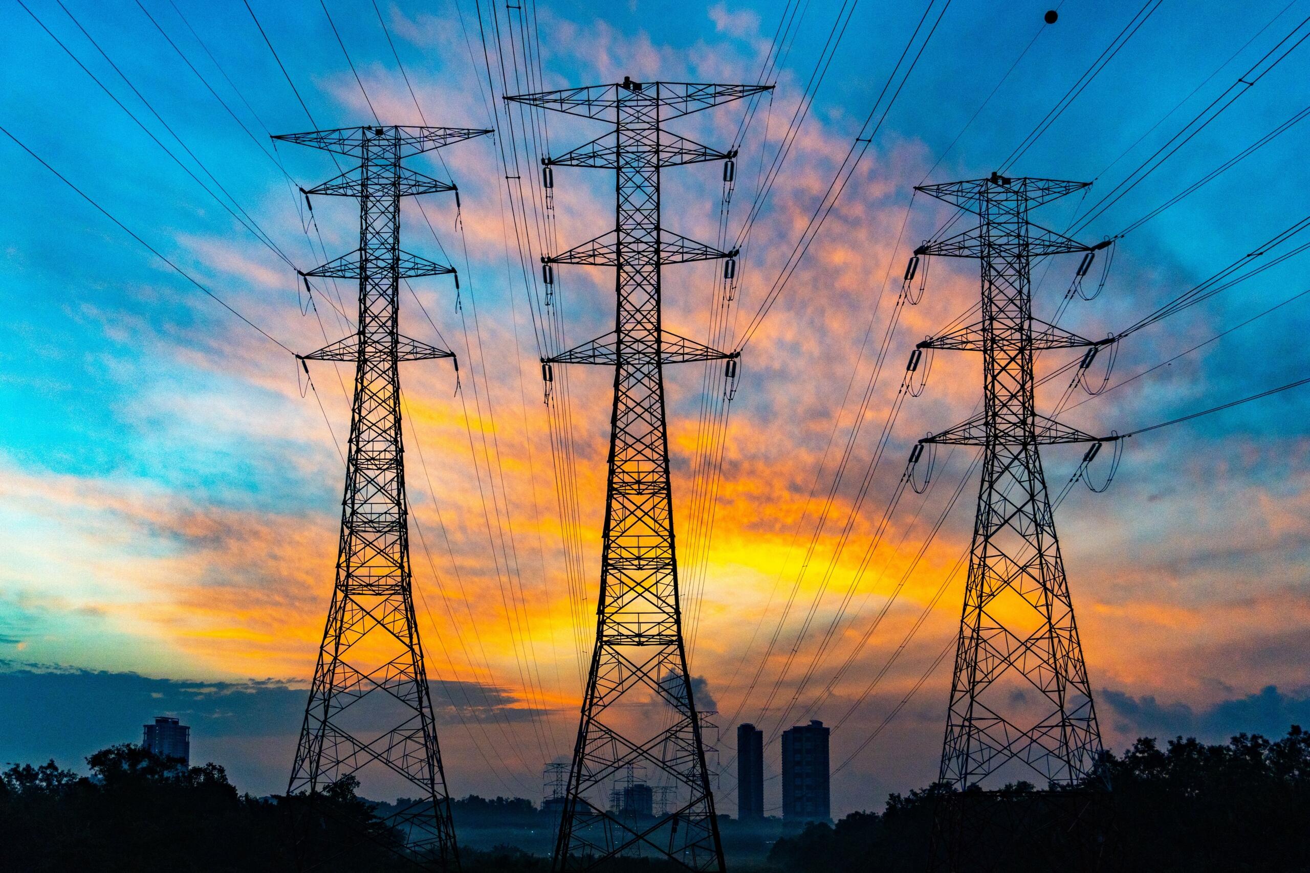Power lines and transmission towers stretch across the landscape at sunset, silhouetted against a warm evening sky.