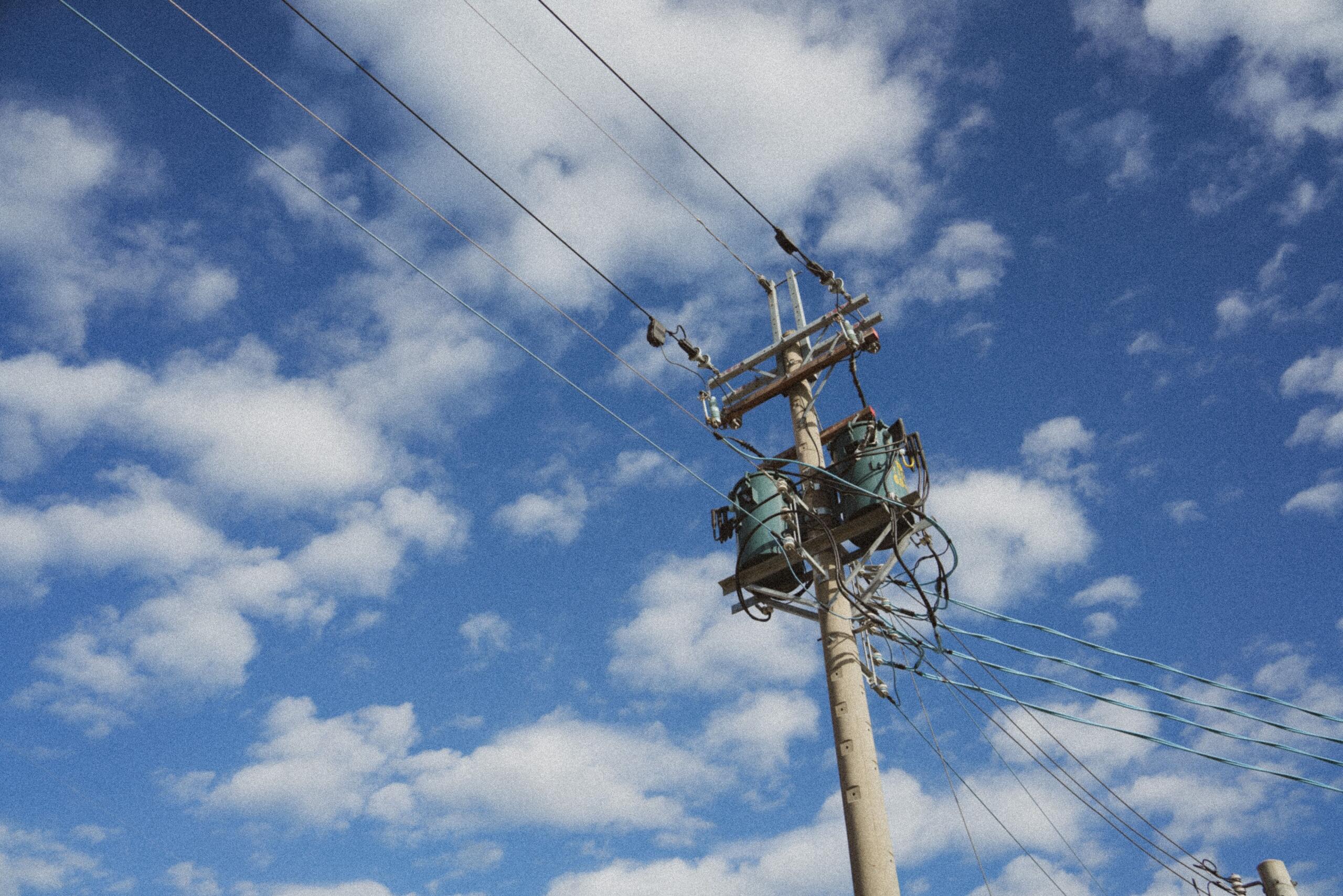 An electrical transformer mounted on a utility pole against a clear blue sky, with power lines extending from the pole.