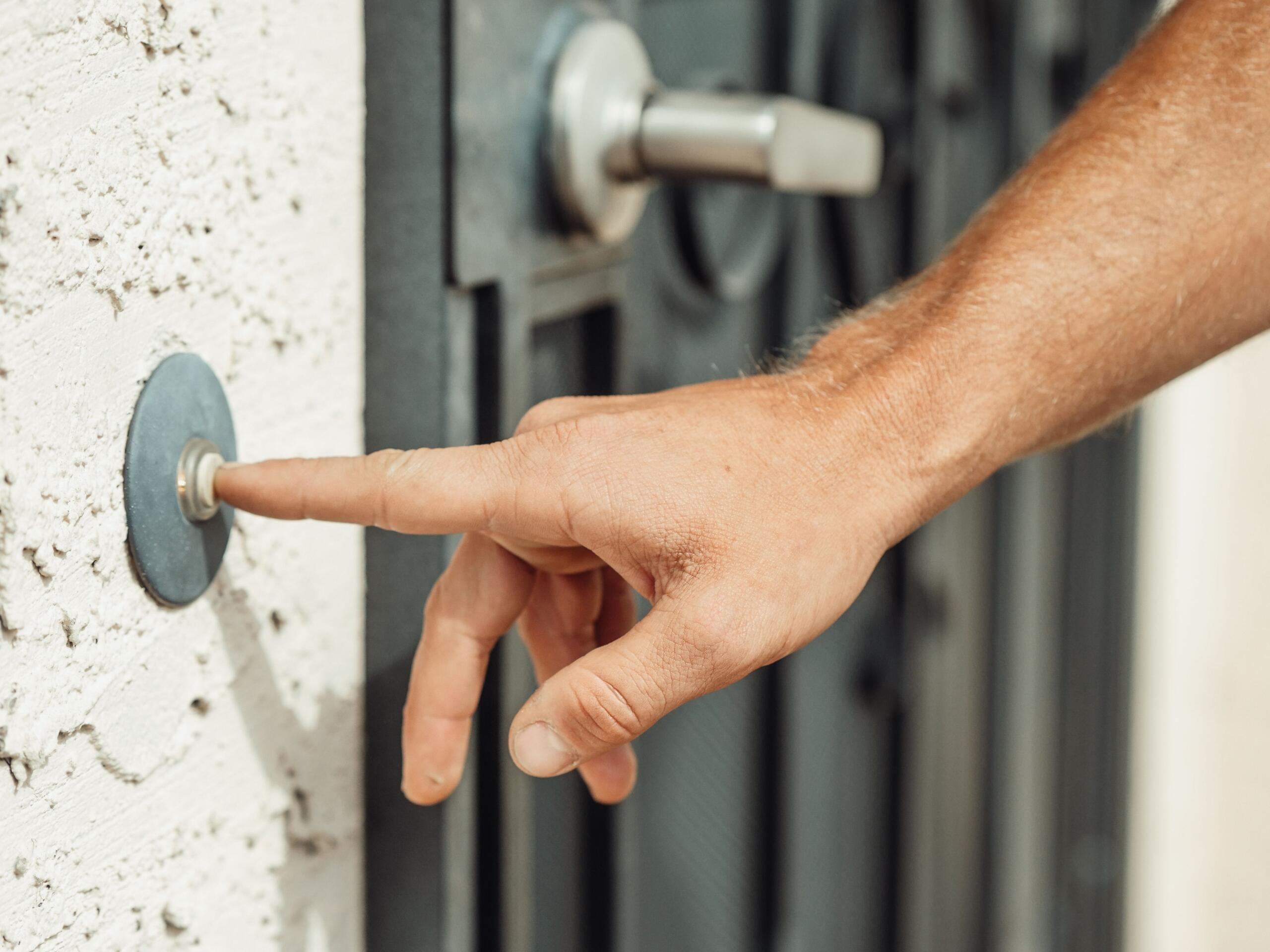A man presses a doorbell button beside a front door with his finger.