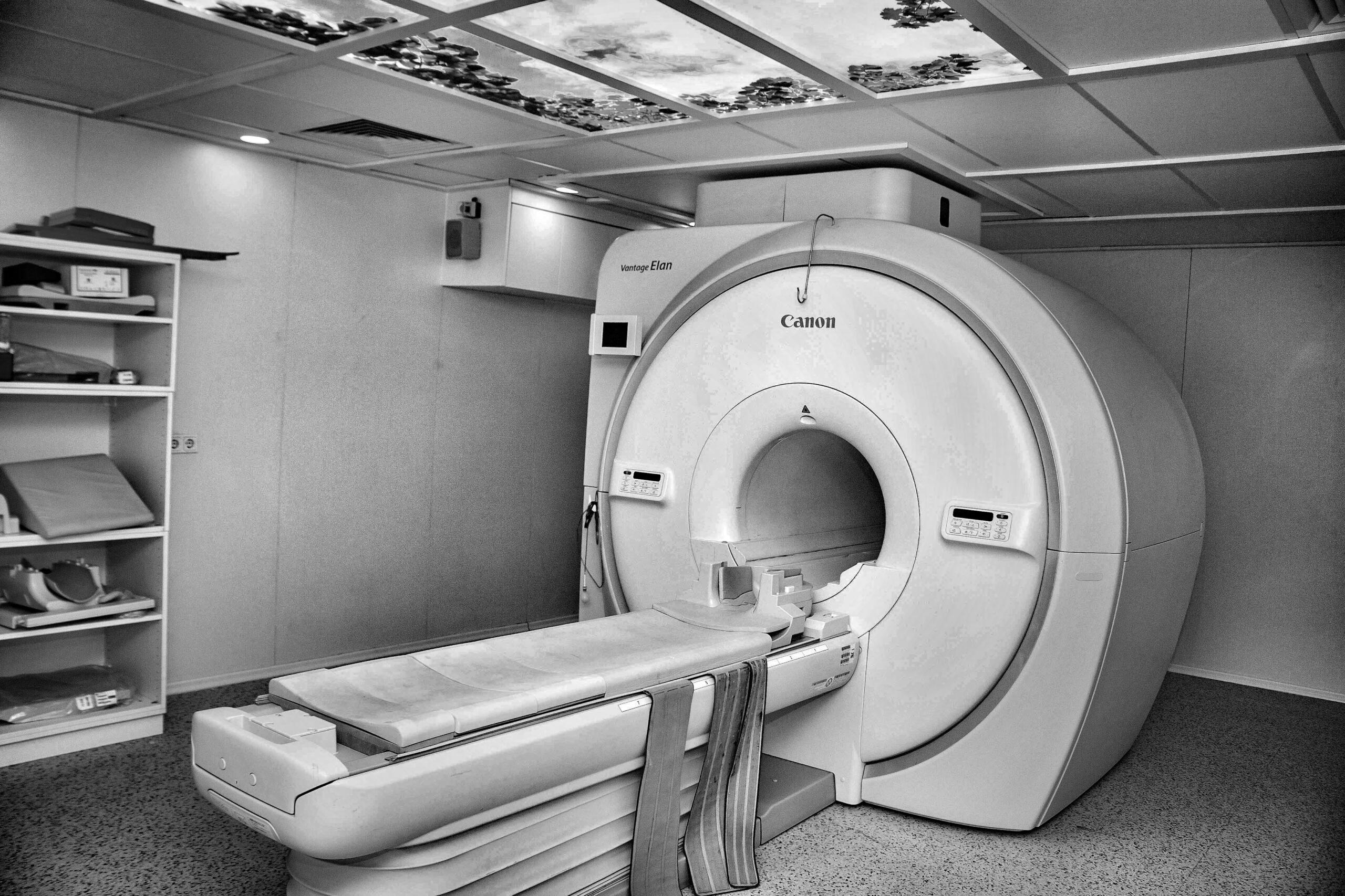 A modern MRI machine in a medical imaging room, featuring a large circular scanner and patient examination table.