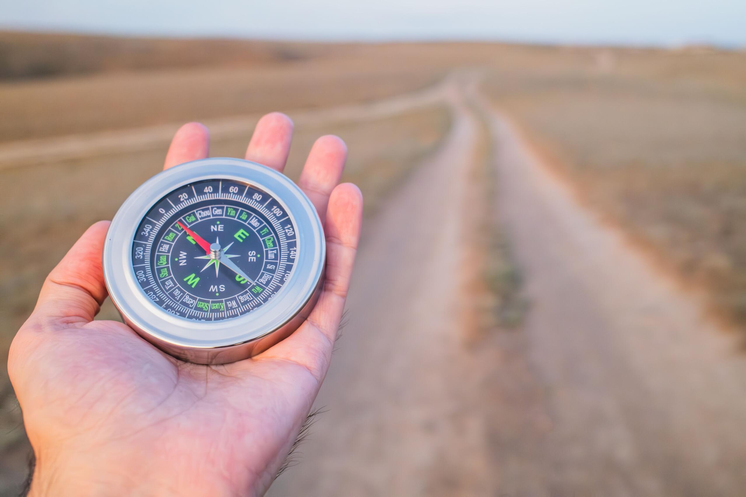 A man holds a compass in his hand while using it to determine direction outdoors.