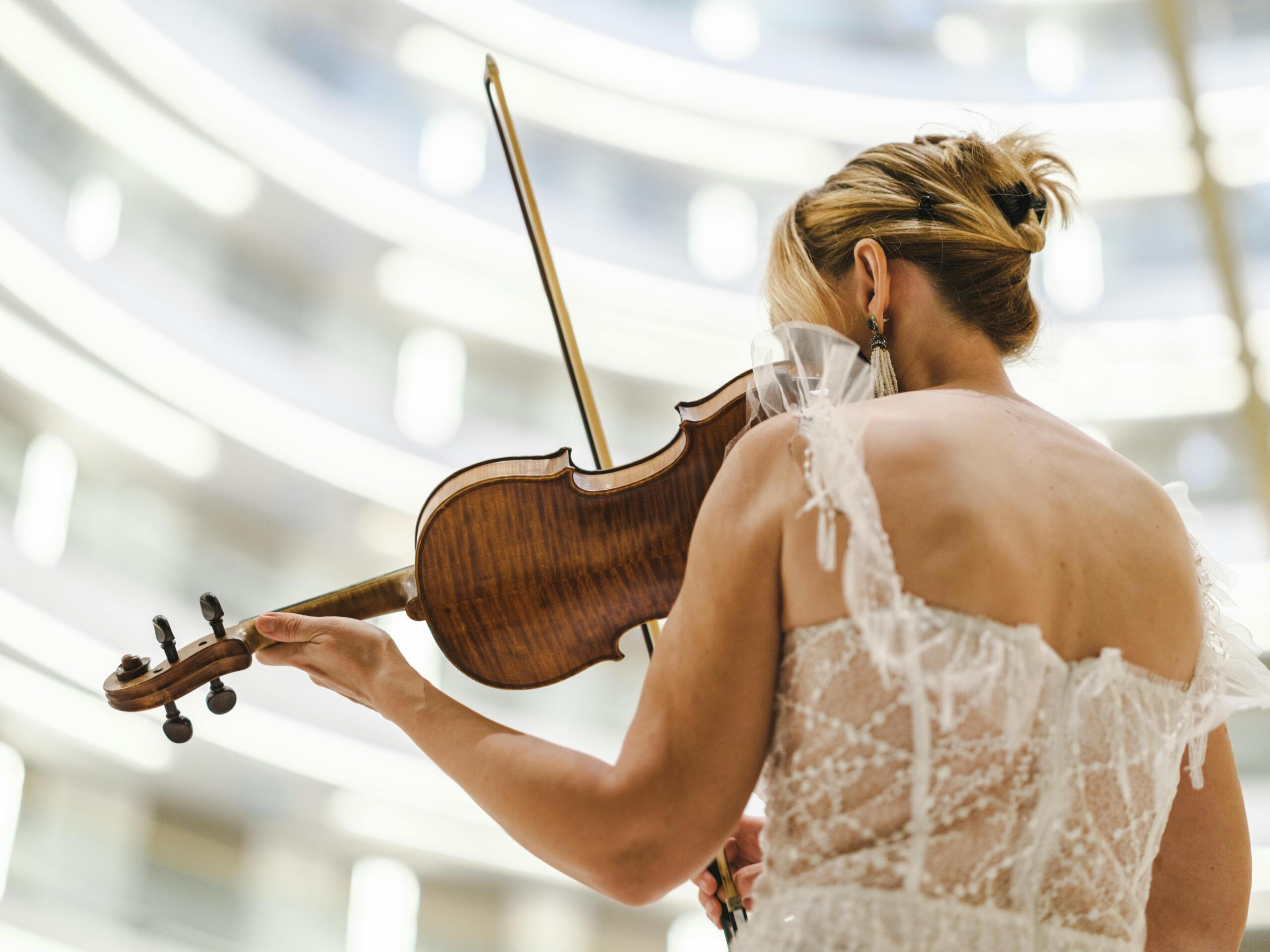a woman in a white dress plays the violin in front of a building.