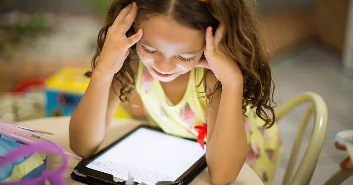 a young girl smiles at a tablet.