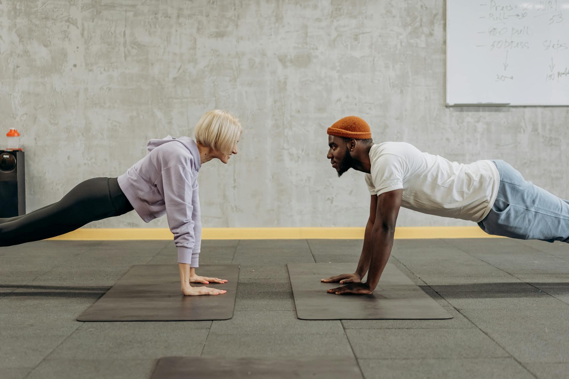 Two individuals perform push-ups on exercise mats in a modern gym, showcasing their focus and dedication to fitness.