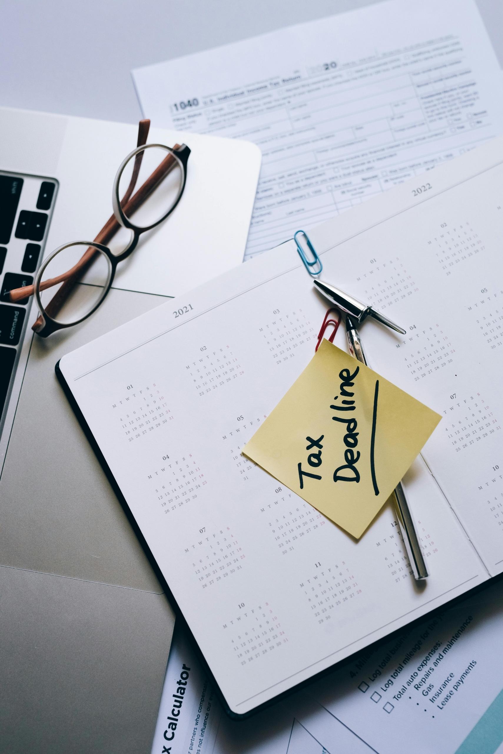 A calendar sitting on the desk with a post it that says "tax time".