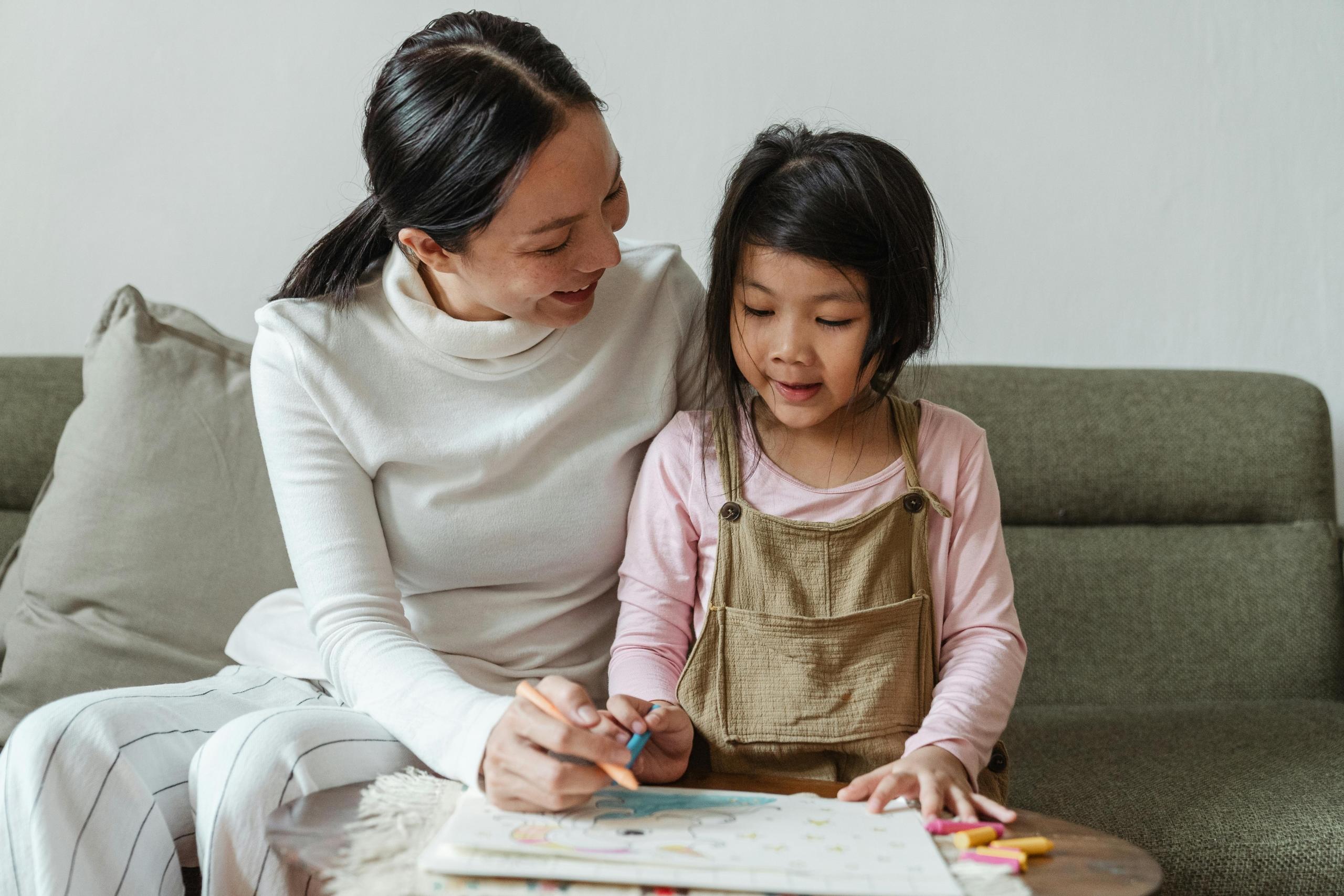 A female tutor helping a young girl learn to draw. 
