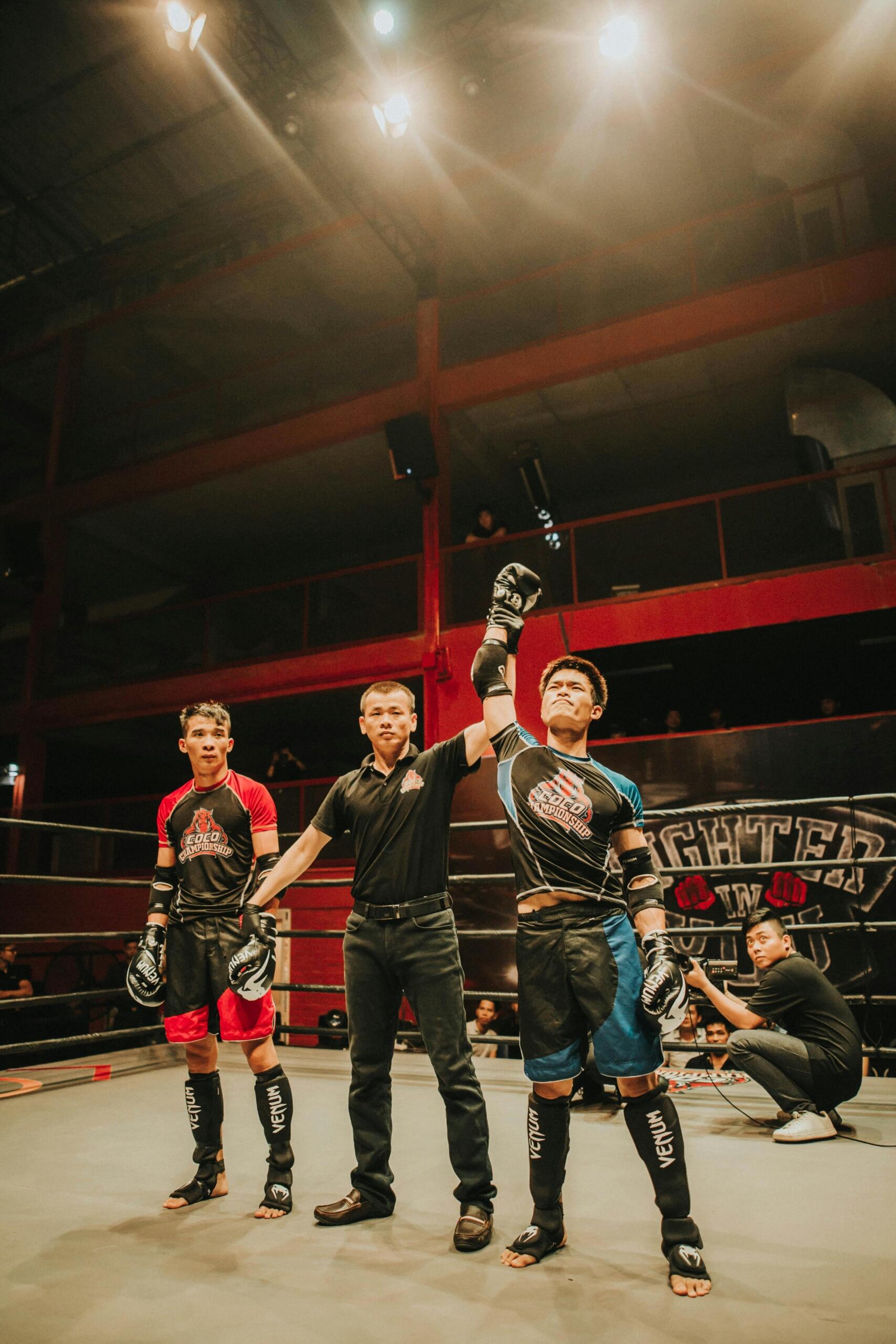 A referee raises the hand of the victorious fighter in a ring after a boxing match, with the opponent standing to the side.