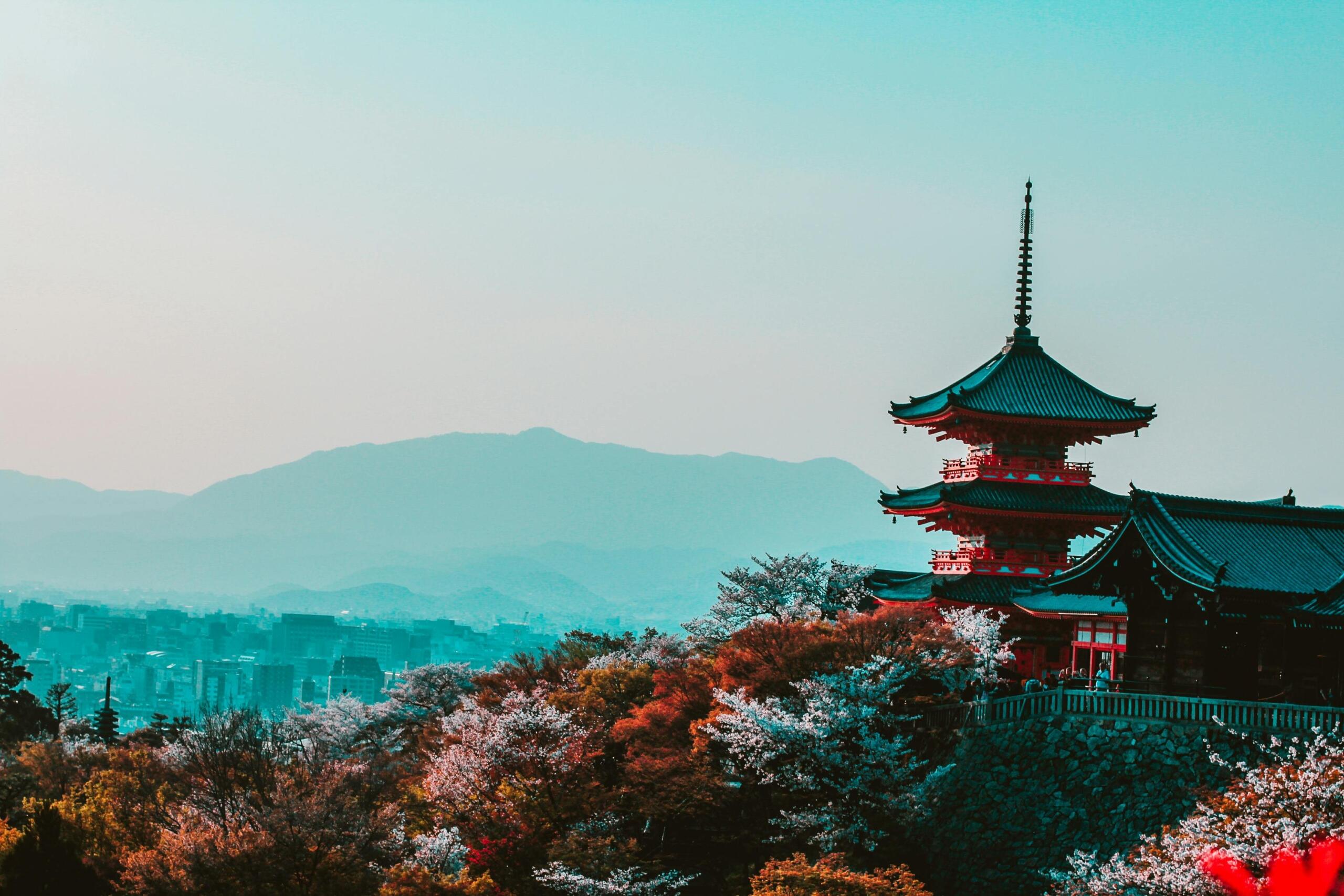 A vibrant red temple in Kyoto, surrounded by lush greenery, showcasing traditional Japanese architecture with curved rooftops and ornate wooden details.