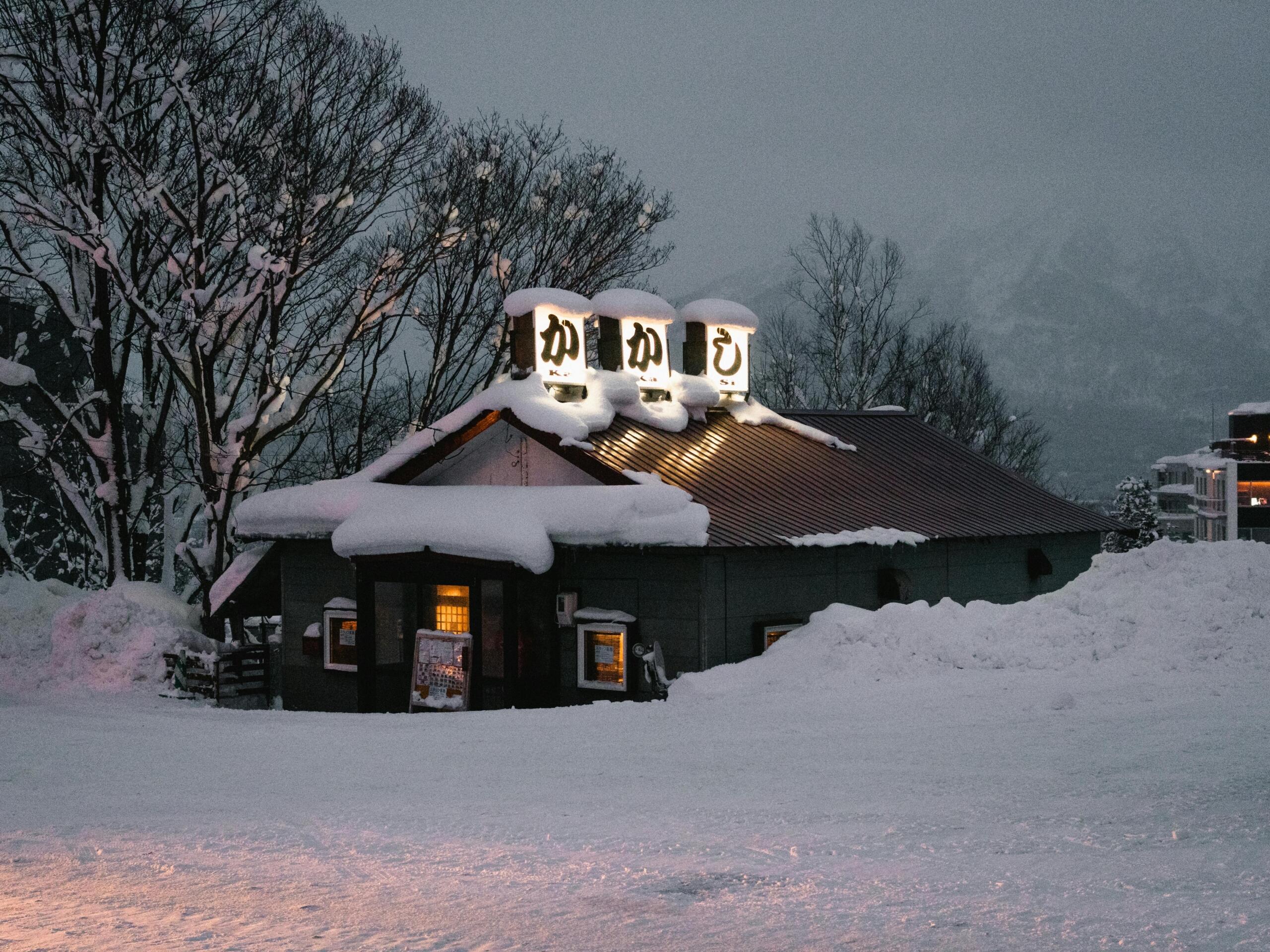 A cozy restaurant in Hokkaido blanketed in snow, with warm light glowing from the windows, creating a serene and inviting winter atmosphere.