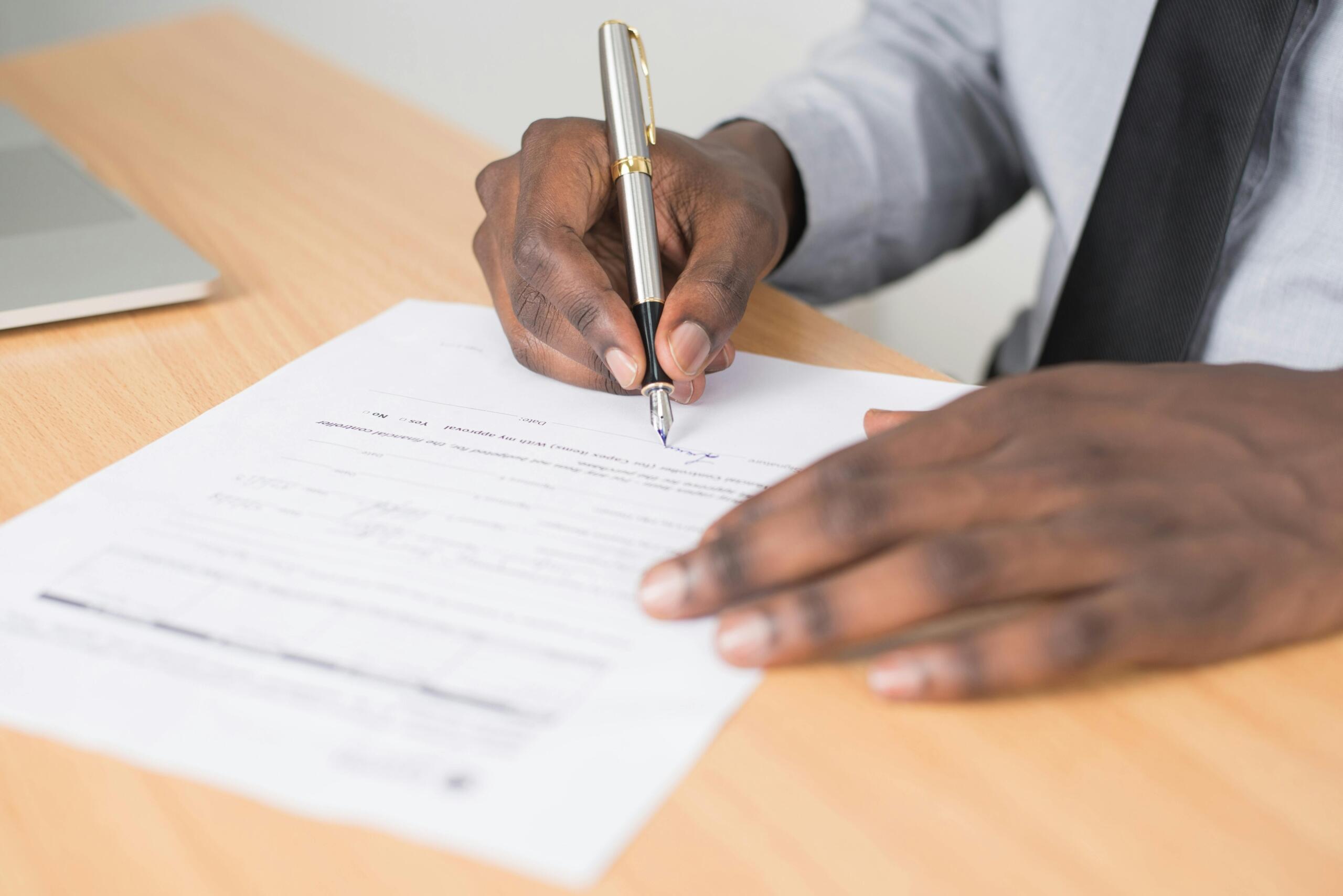 Close-up of a man’s hand holding a pen while filling out an application form on a desk.