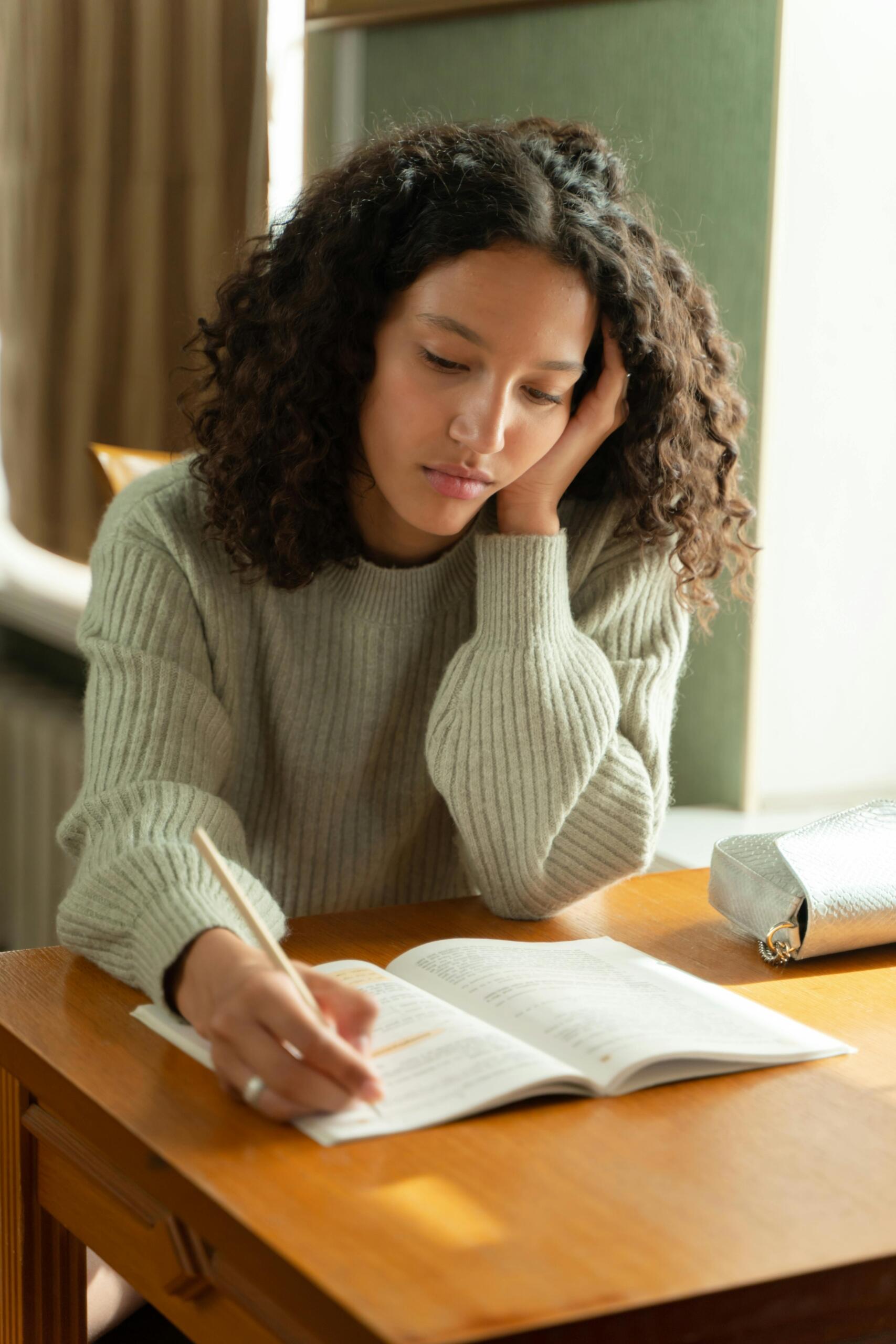 A young woman looks thoughtfully at a notebook as she does her school work. Source: Yaroslav Shuraev.